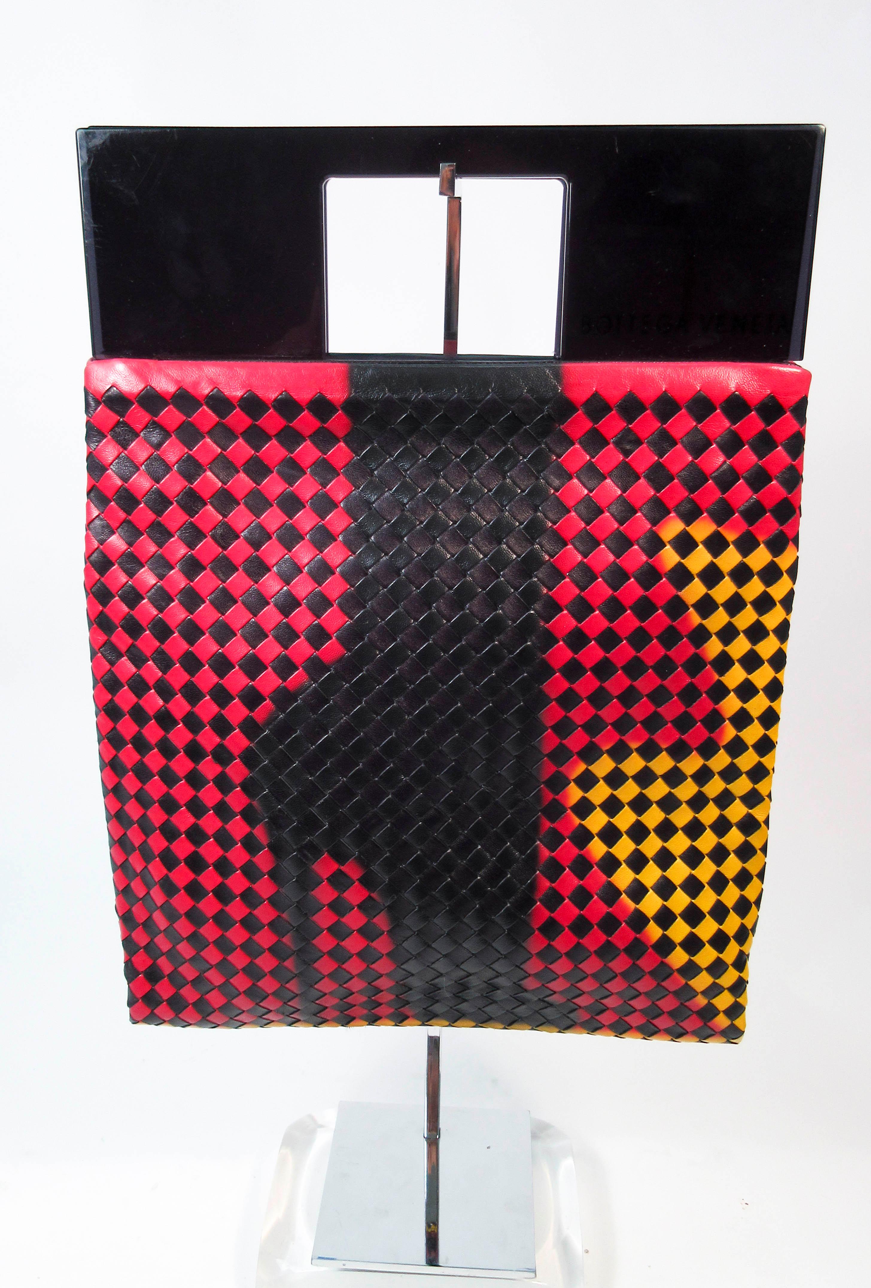 This Bottega Veneta purse is composed of a beautiful black, yellow, and red woven leather with a high heel design. Features a shopper shape with a plastic upper frame and suede lining. There is an interior zipper pocket. In excellent almost new