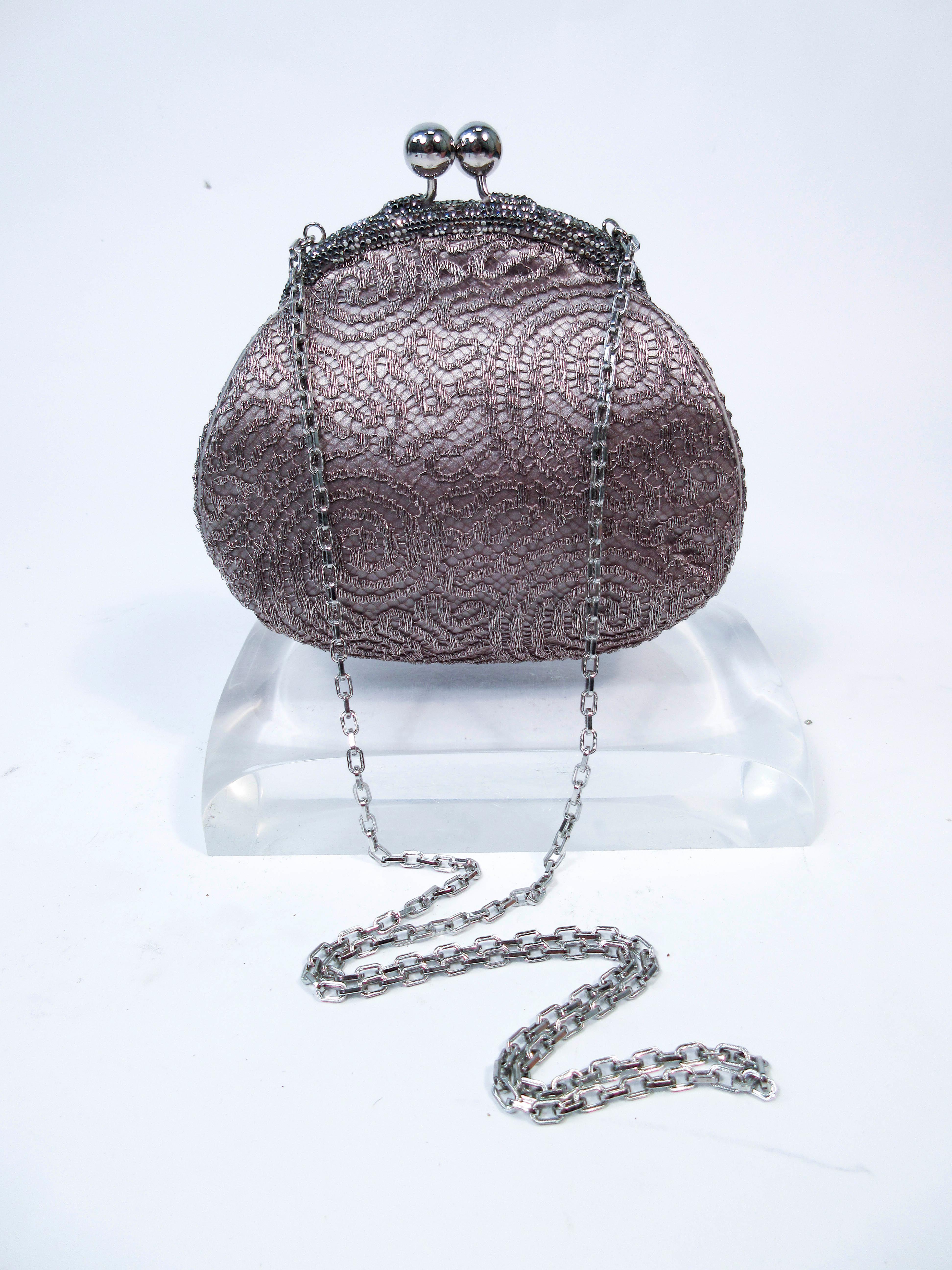 This Judith Leiber purse is composed of a metallic silver-tone taupe lame.  Features a silver-tone frame with rhinestone accents and an interior pocket. In excellent almost new pre-owned condition (some signs of wear due to age, see photos). Sold