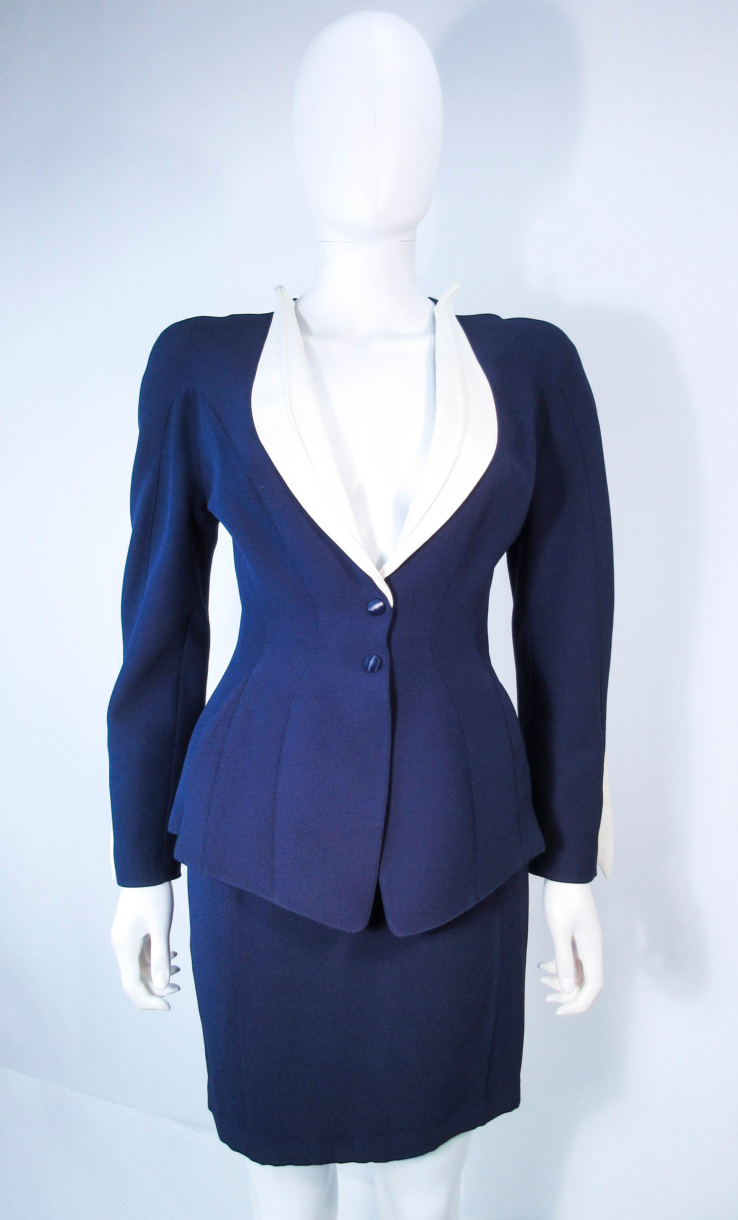 This Theirry Mugler skirt suit is composed of a viscose rayon blend.. The jacket features a peplum design with snap front closures, a contrasting white collar, and shoulder cut out details. The classic pencil style skirt features a zipper closure..