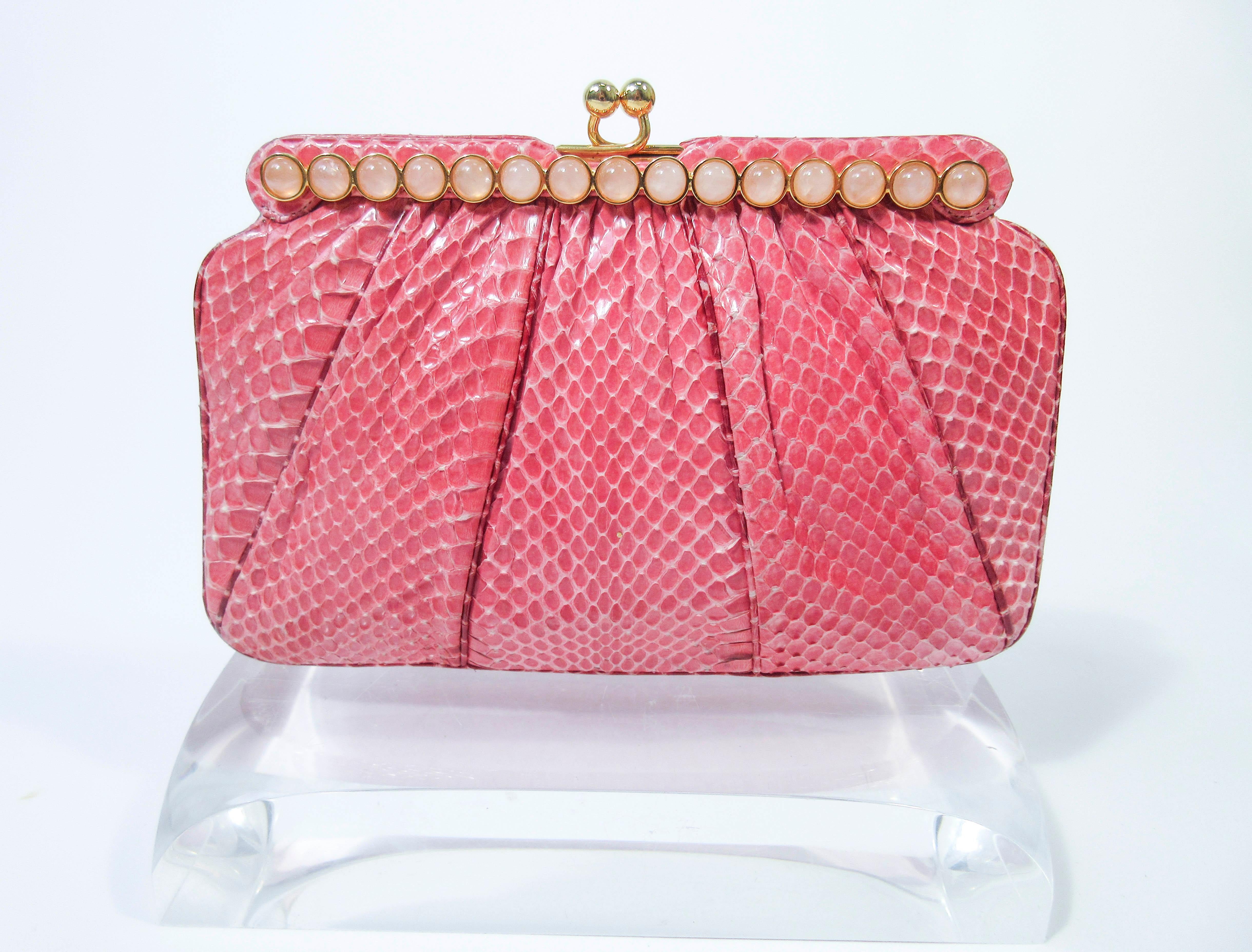 This Judith Leiber purse is composed of a pink snakeskin. Features a bar style frame with cabochon stone accents and gold hardware. There is an interior pocket and two slide pockets. In excellent 'like new' pre-owned condition (some signs of wear