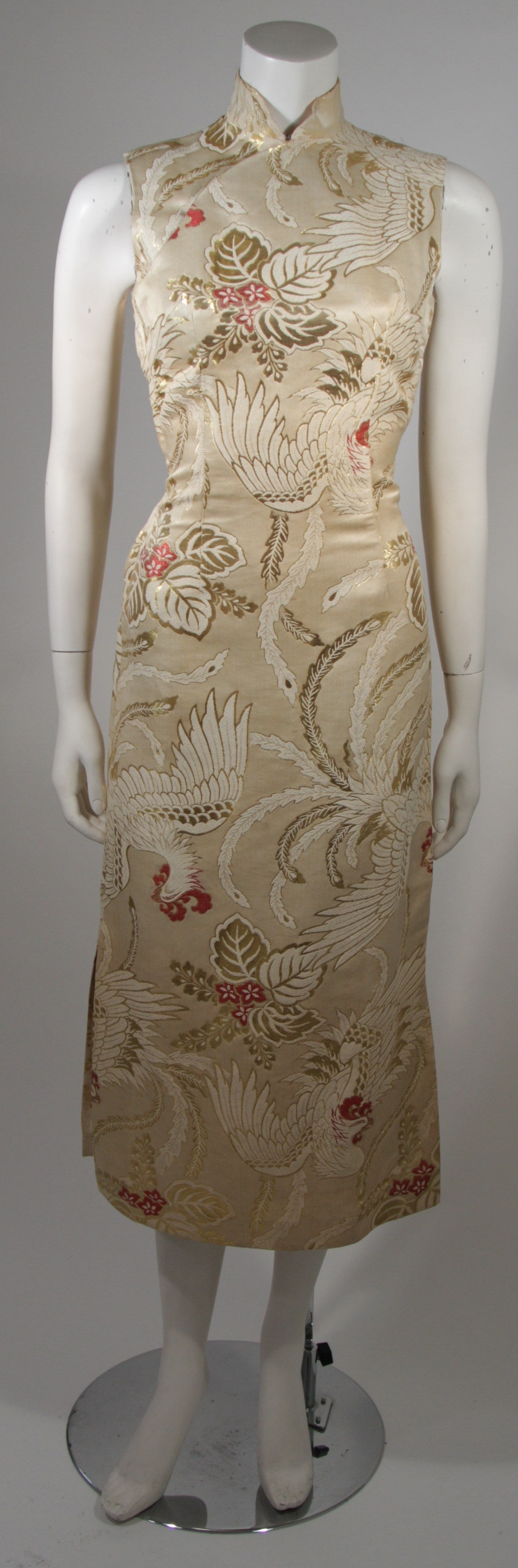 Este vestido de cóctel de los años 50 hecho a medida está compuesto por un brocado de seda marfil, crema y dorado con detalles rojos. El vestido presenta un estampado de Fénix. Tiene un cierre de cremallera lateral metálica y escote mandarín y