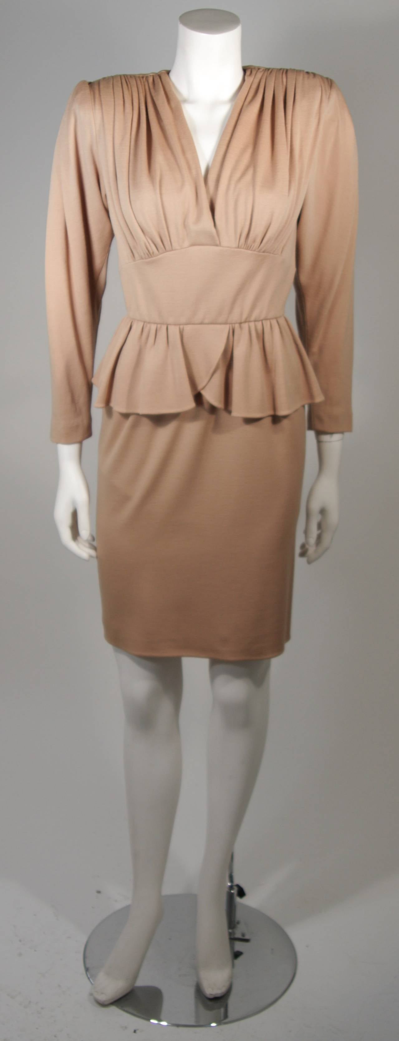 This Nolan Miller attributed ensemble is composed of a camel wool jersey. The cocktail dress is an above the knee style with peplum and gathered shoulders. The dress has a center back zipper. The cape has three center front neck closures. This is a