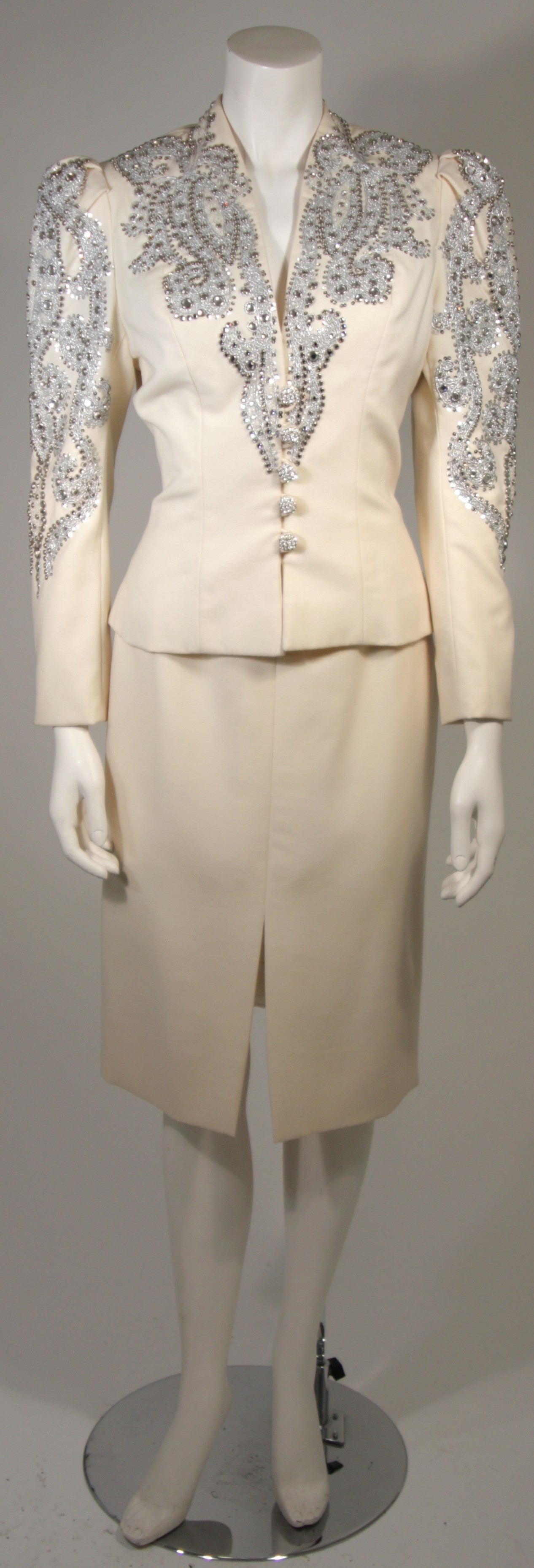 This Nolan Miller set is composed of an Ivory wool which is embellished with rhinestones and silver lace. The blazer features center front rhinestone buttons and a peplum flare design at the waist. In excellent condition.

Measures
