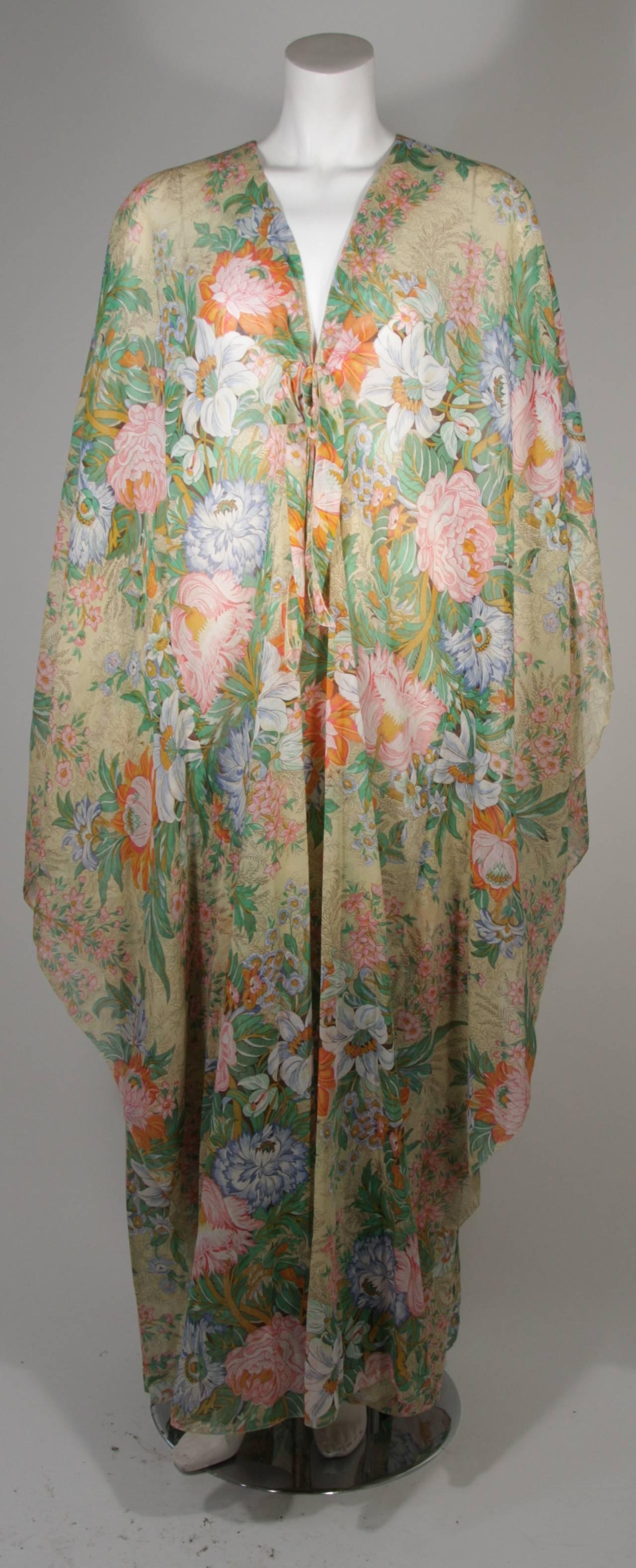 This Lucie Ann kaftan is composed of a lightweight cotton featuring a floral motif in melodic hues of brown, nude, orange, and green. An absolutely wonderful textile print of blooming flowers. In excellent condition. There is a center front tie at