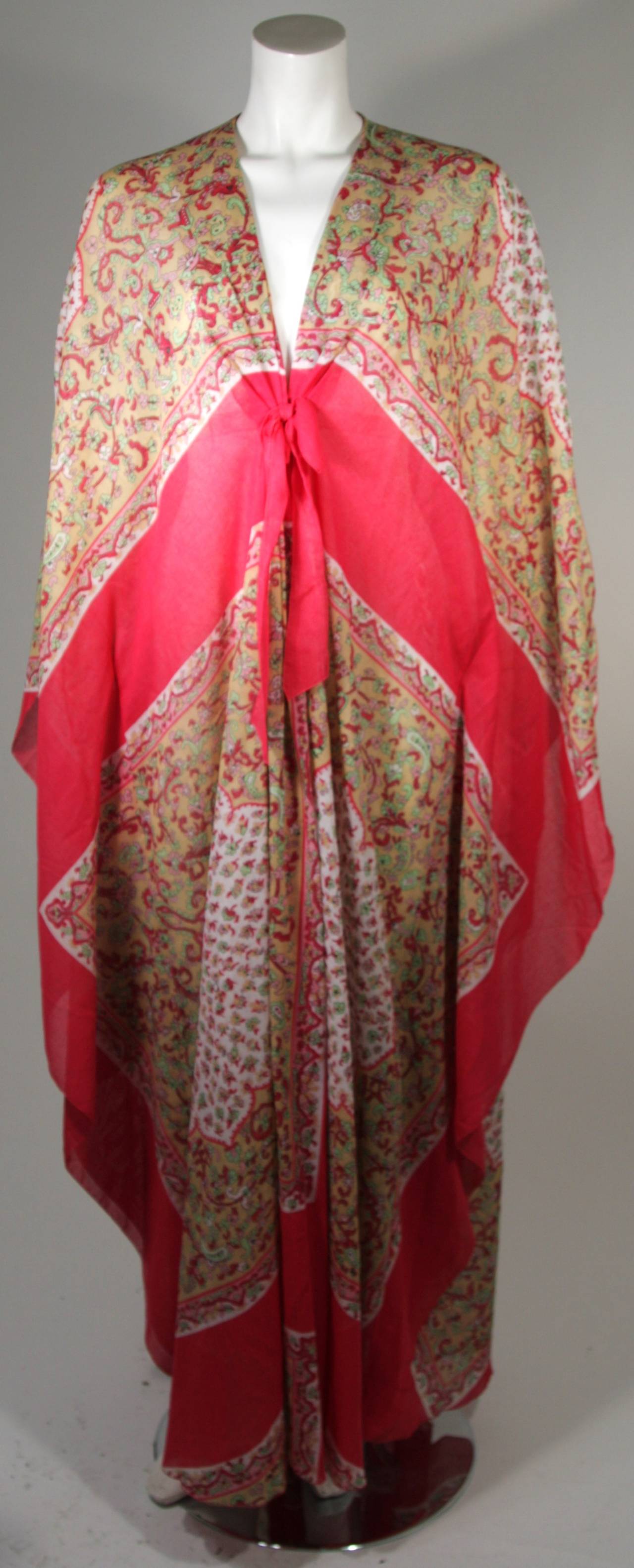 This Lucie Ann kaftan is composed of a lightweight cotton featuring a floral motif in hues of red, yellow, white, and green. An absolutely wonderful textile print. In excellent condition. There is a center front tie at the bust, and elastic interior