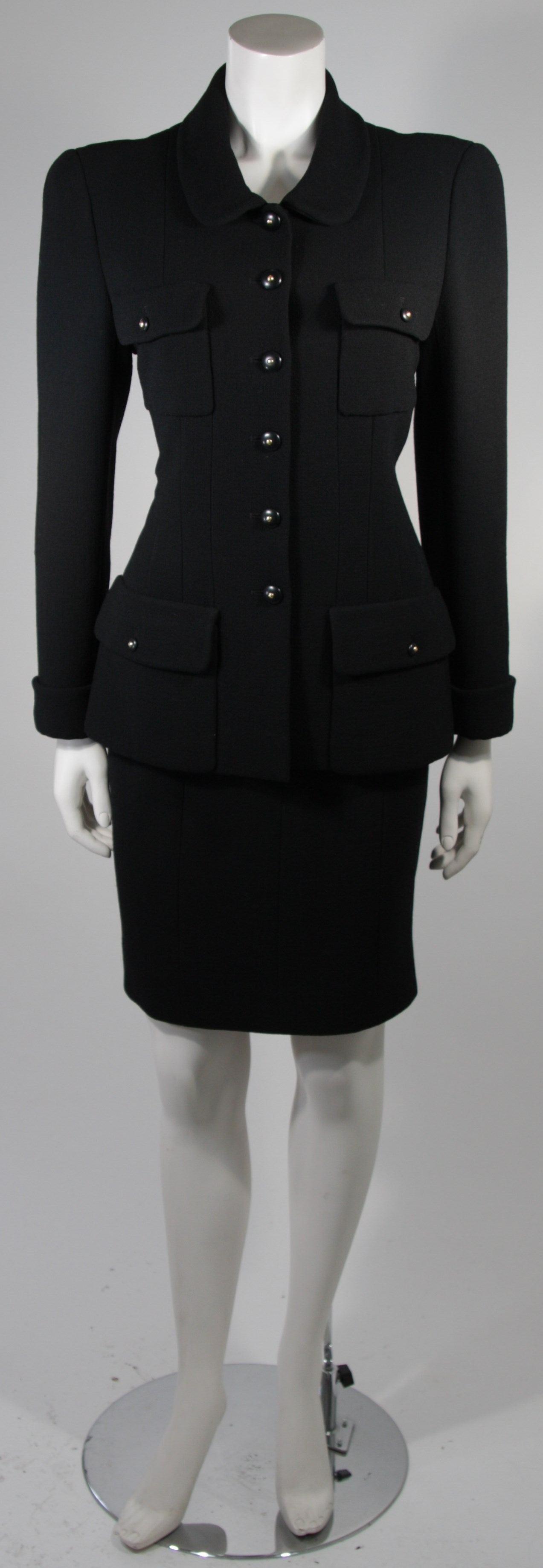 This Chanel skirt suit is available for viewing at our Beverly Hills Boutique. We offer a large selection of evening gowns and luxury garments.

This suit is composed of a black wool crepe. The jacket features four front pockets and a Peter Pan