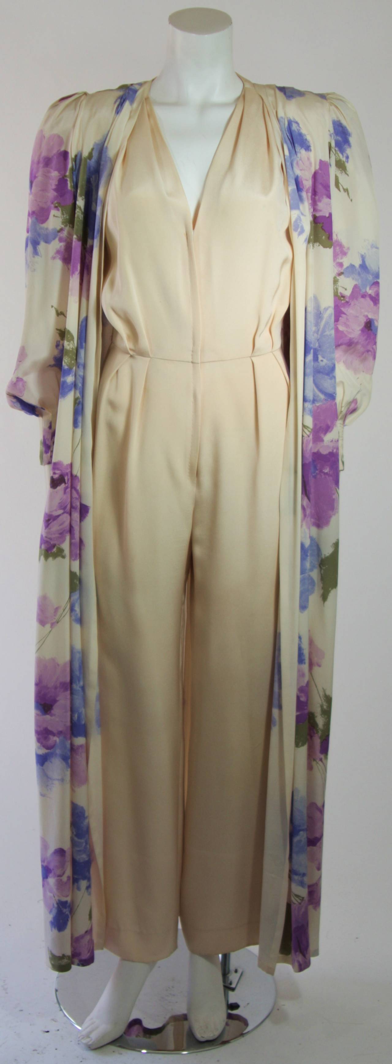 This Nolan Miller attributed set is composed of silk. The jumpsuit is an off white cream hued silk and features pleat details. There is a center front zipper closure. The jacket is an open style with a water color floral motif in blue and purple