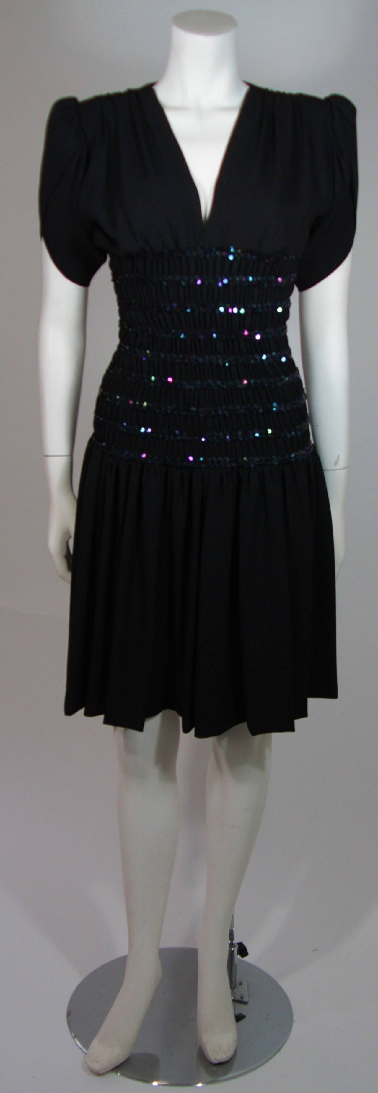 This Yves Saint Laurent cocktail dress is composed of a black crepe and features a smocked waistline with iridescent navy sequins. The sleeves are a drape style and there are gathers at the shoulders. Pull over style. Made in France.  

**Please