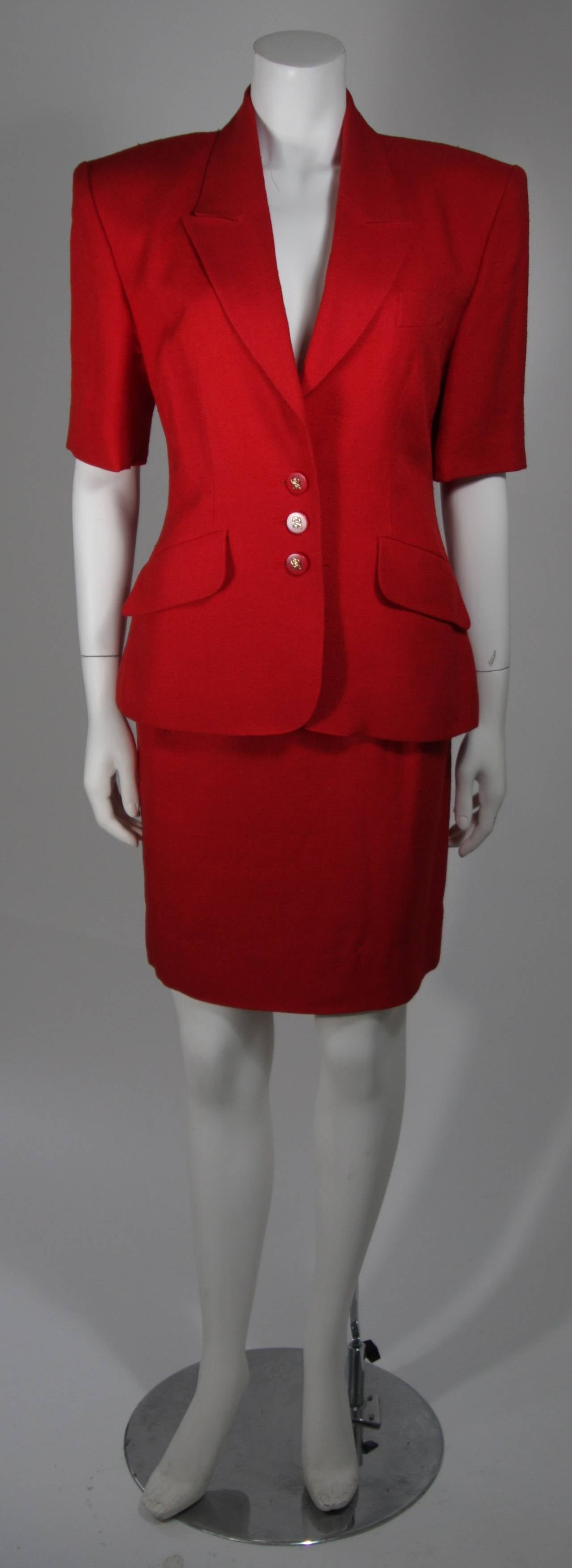 This Hermes Two Piece short sleeve red classically styled jacket with working angled flap pockets, three red buttons at waist and on the sleeve backs with golden H details. 
The skirt features a fitted waistband with pleat front, a red metal side