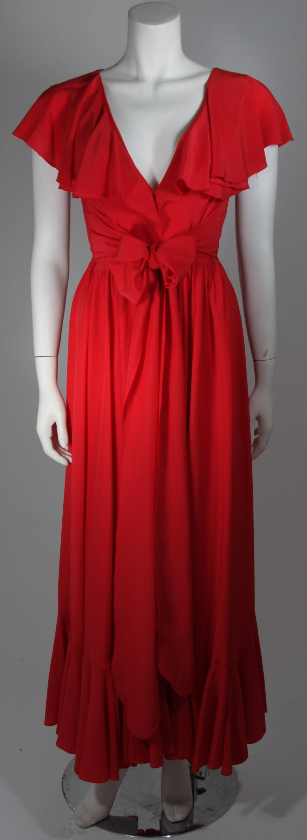 This Oscar De La Renta gown is composed of a striking shade of red silk with a chiffon under layer. The silk is draped in a cascading style and is accented with a waist wrap, which can be worn to the front or back. There are center front closures.