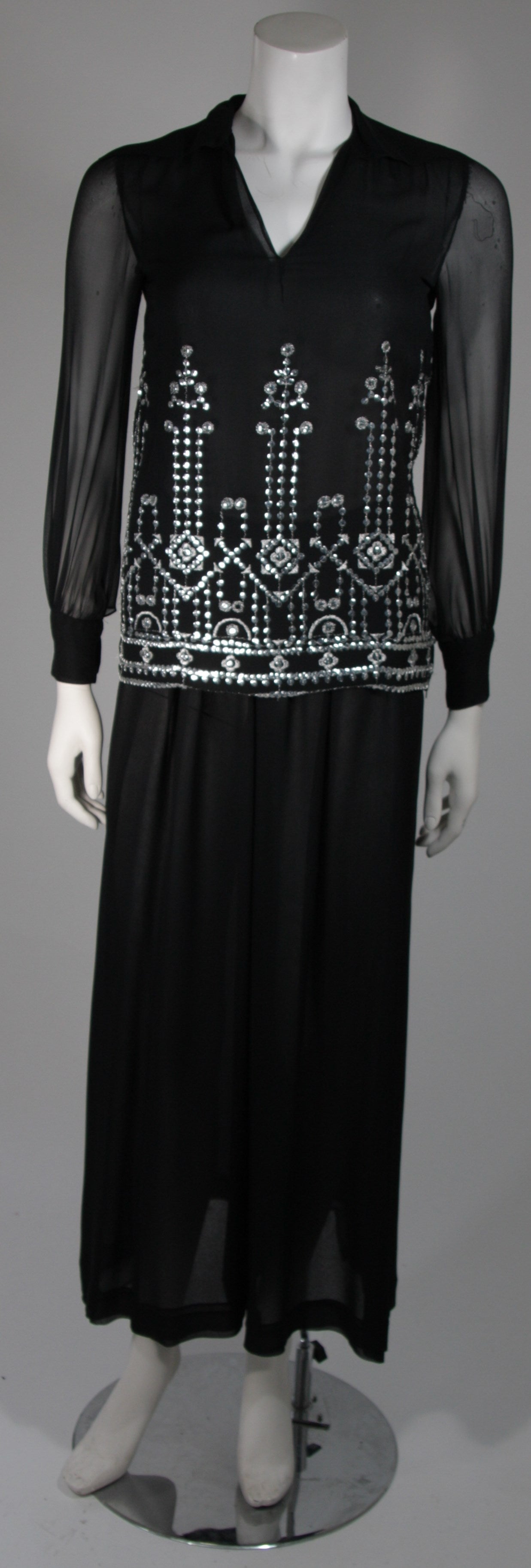 This Christian Dior ensemble is composed of a black silk chiffon. The tunic style top with collar features a side zipper and is embellished with silver sequin accents. The pants are a chic wide leg style with an elastic waist. Made in France.