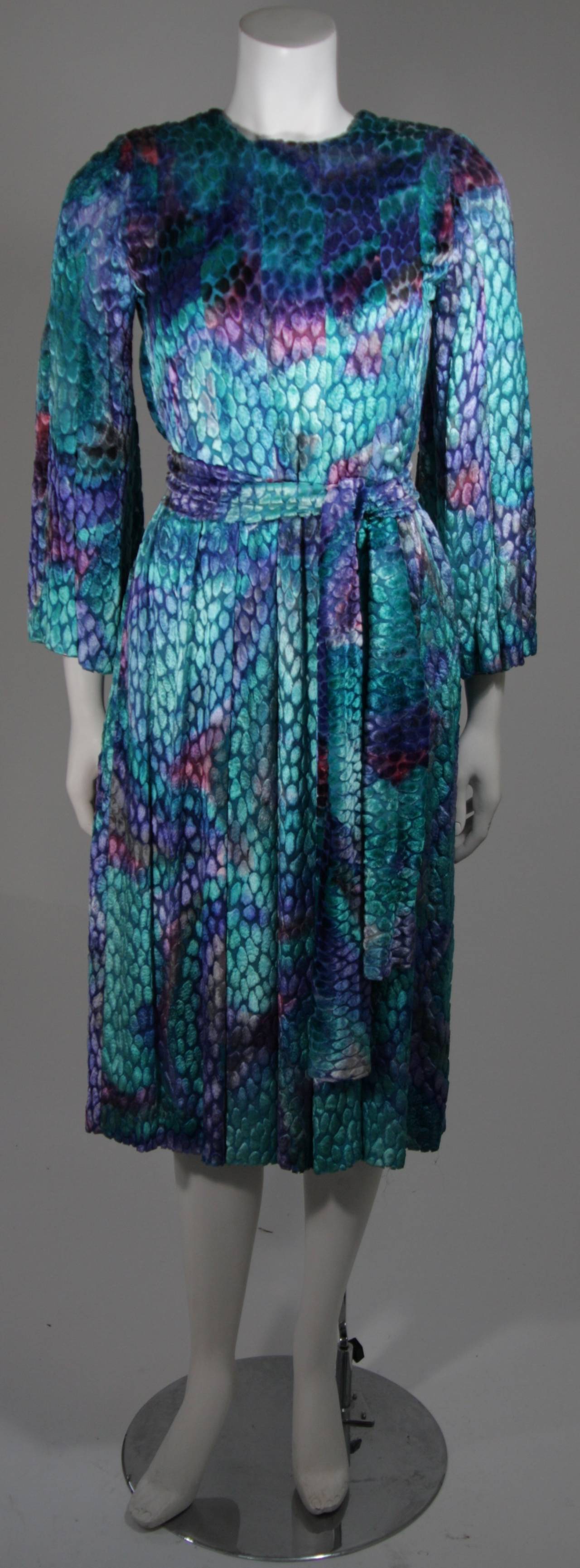 This Pauline Trigere dress is composed of a spectacular mutli-tone velvet burn out in turquoise with splashes of magenta throughout. The dress features a flared sleeve and there is a center back zipper. The wrap may be fashioned in anyway you