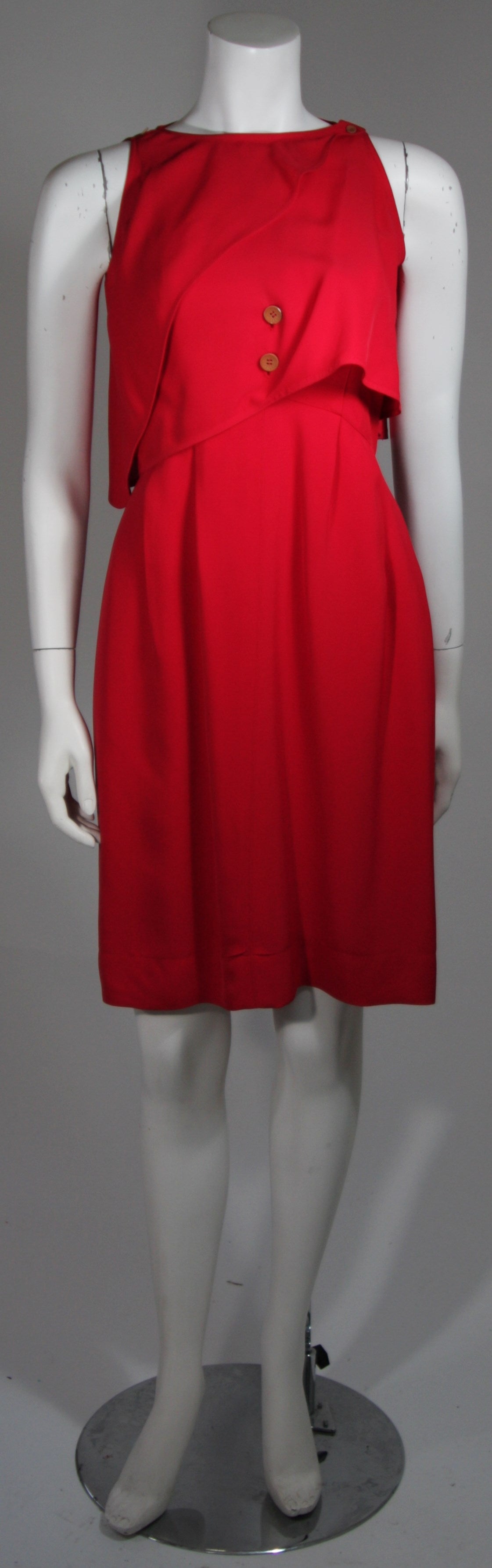 This Fendi dress is composed of a vibrant red fabric. The dress is designed in a fashion to accentuate the use of buttons, one can remove the caplet for a classic strap style dress or let it remain for a flowing effect. There is a zipper closure and