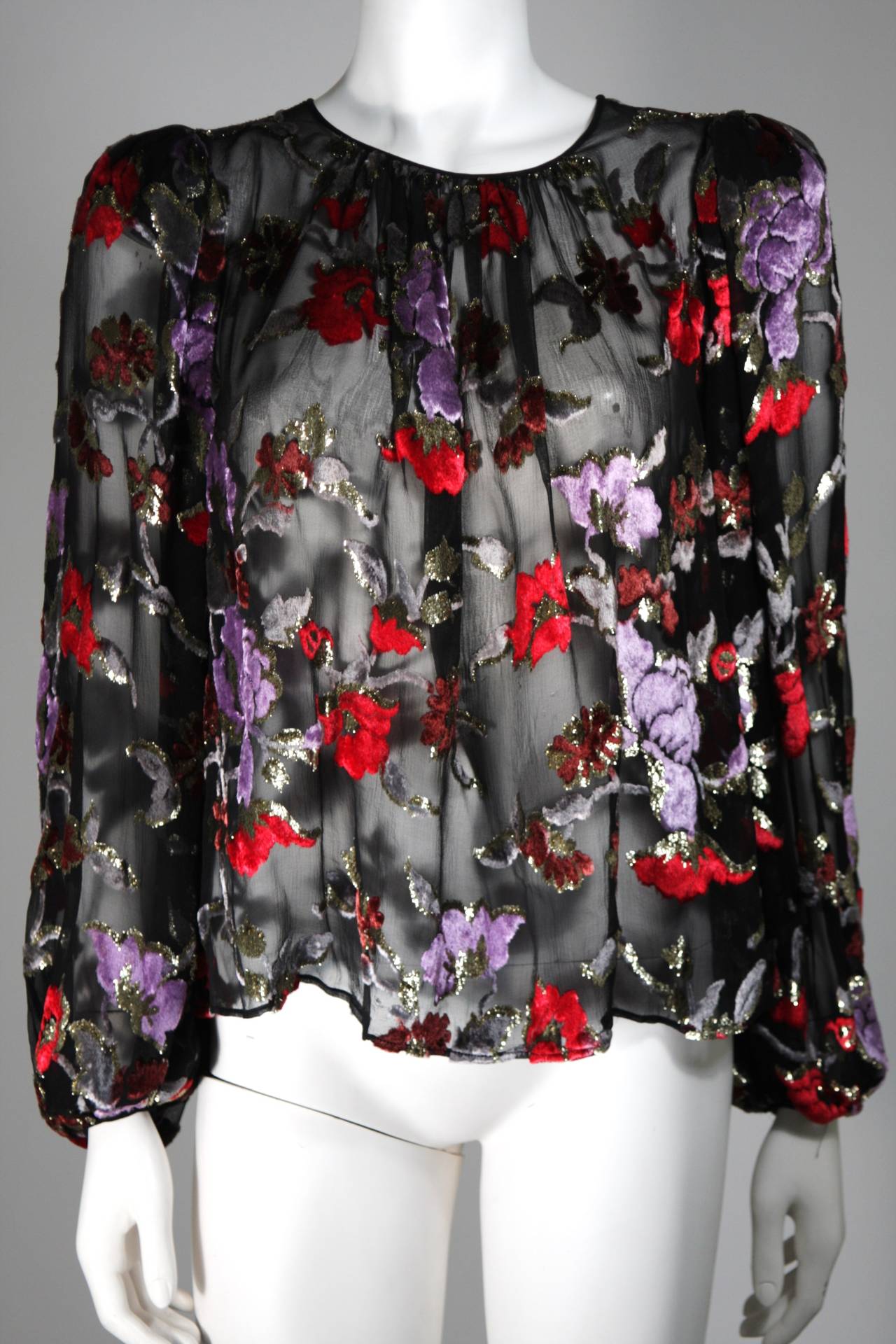 Gorgeous sheer black silk chiffon evening blouse by Oscar de la Renta with rich red and purple lurex flowers throughout. Lightly padded shoulders, flowing sleeves, with a fitted hidden hook and eye closure at the wrists. The blouse fastens at the