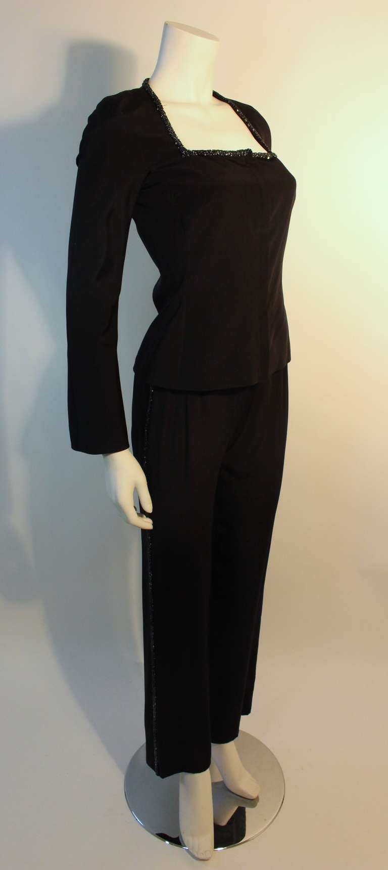 Gianni Versace Couture two piece black silk, long sleeve (with underarm gusset), square neck jacket with hidden front zipper. The neckline is subtly embellished with metallic black caviar beads and a smattering of fine silver sequins. 
The trousers