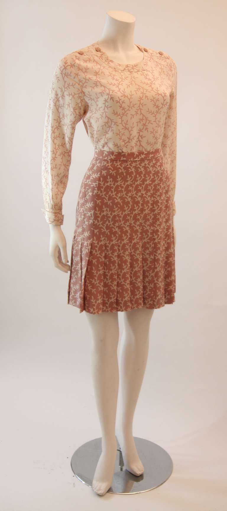 This is a charming Chanel skirt set. The set is a beautiful hue of mauve pink, it comes with three pieces, a jacket, a blouse, and a wonderfully pleated skirt. The Jacket features a five button closure  and two front pockets. The skirt falls