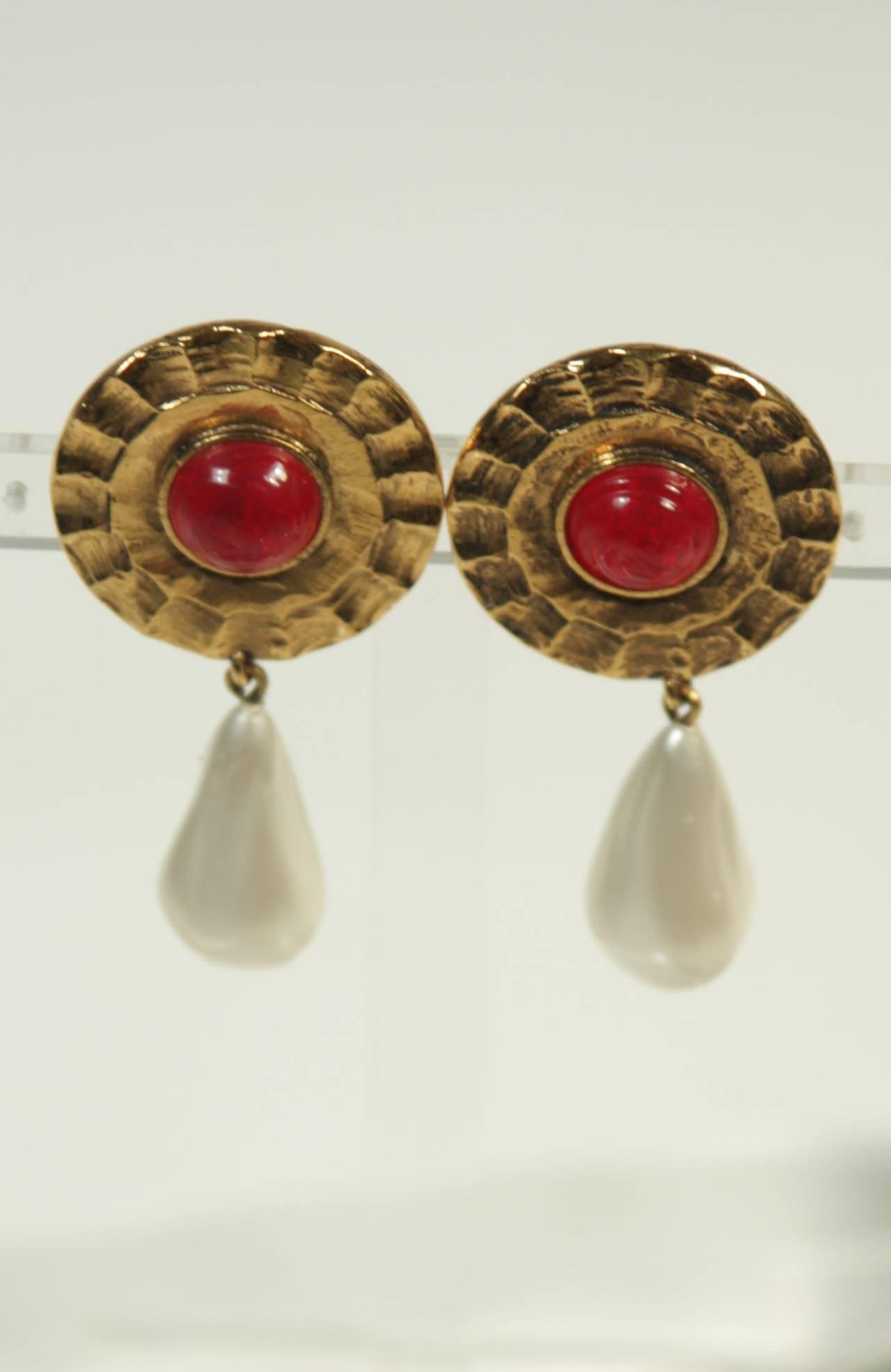 These vintage Chanel earrings are composed of a gold tone material and feature a pearl drop with red poured glass in the center. They are clip on style. In excellent condition, come with original box.
Signed: CHANEL, possibly by Robert Goossens as