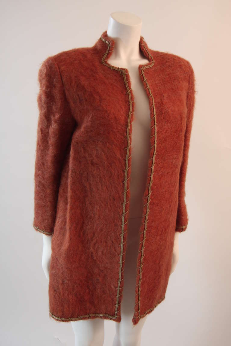This is a May McFadden coat. It is composed of a Mohair blend and features gold trimming. The coat is in a wonderful spiced pumpkin hue. 

Measures (Approximately)
Size 6
Length: 34