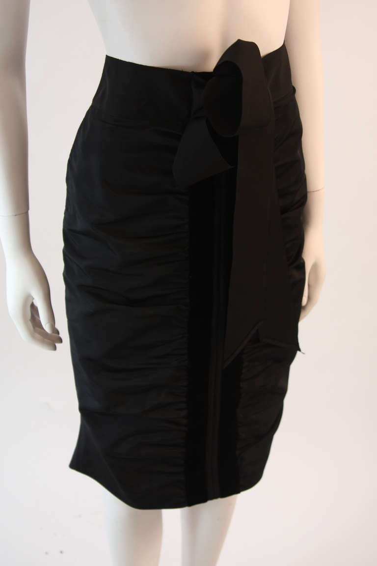 This is a Yves Saint Laurent skirt. It is composed of a nylon material with a center front ruched detail trimmed by velvet. There is a wrap feature which can be worn to the front or back, This is a sharp and beautiful addition to any wardrobe.