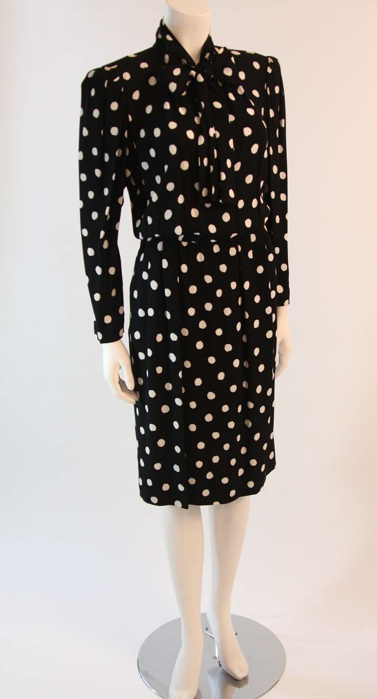This is a wonderful Yves St. Laurent. This dress is an amazing black and white polka dot print. It features a side zipper, two side pockets,  front button closure, tie neck, and darts/pleats at the sleeves and waist, and zippers at the wrists. The