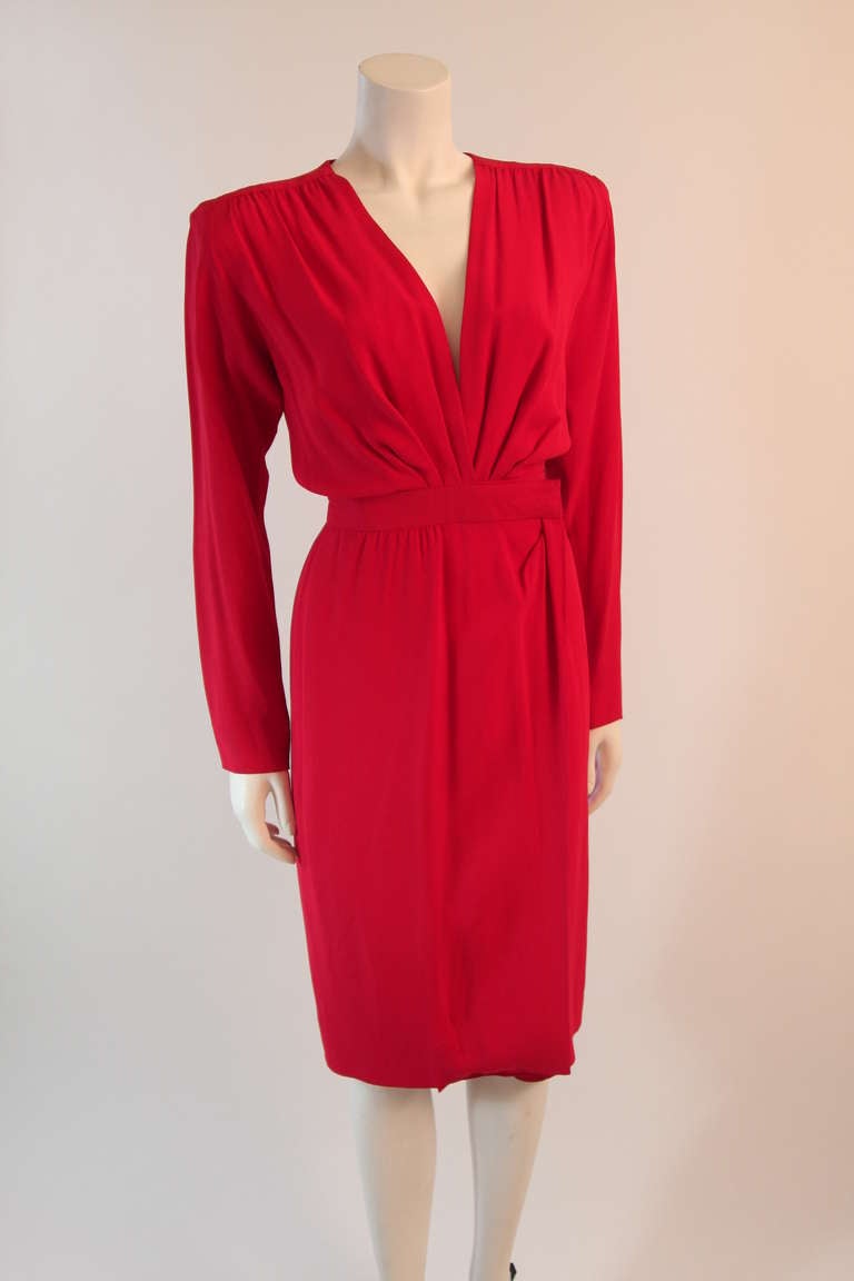 This is an absolutely fabulous Saint Laurent Rive Gauche dress. The wonderful eye catching cardinal red is complimented by a deep plunging draped neckline. The wrap style waist fastens with one hook on the inside and one at the waist band left of
