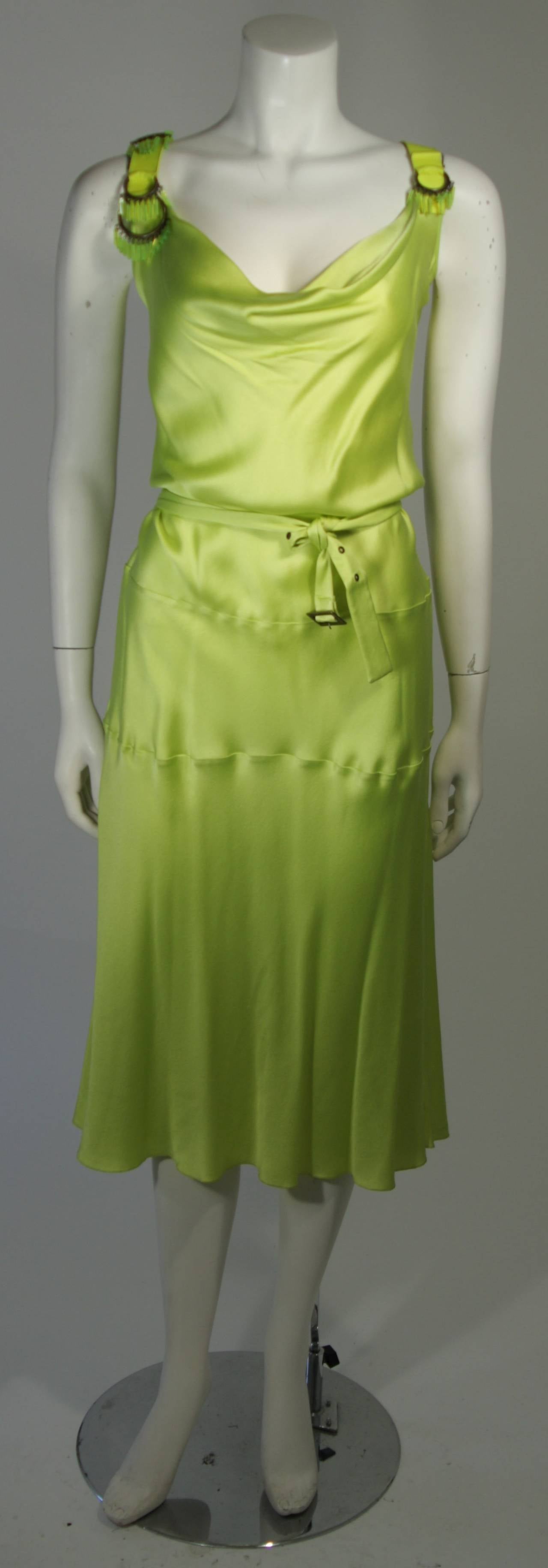 This is a sexy evening cocktail dress made by John Galiano. It is made from a lime green silk charmeuse, bias cut, drapes at the bust and the back. There is a matching belt that fits low on the waist. There are leather straps and metal rings with