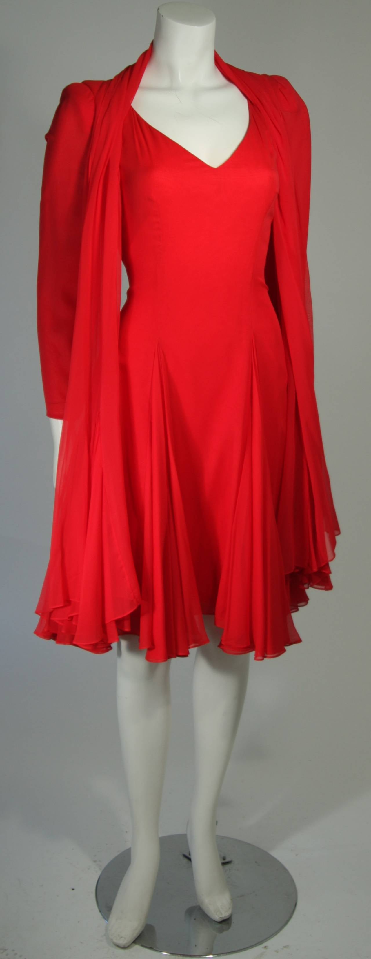 This Travilla cocktail dress is composed of a fabulous red silk chiffon and is coupled with a matching shawl. The dress features a body skimming design which is accented by godets at the skirt, the shawl has the same flared styling. There is a