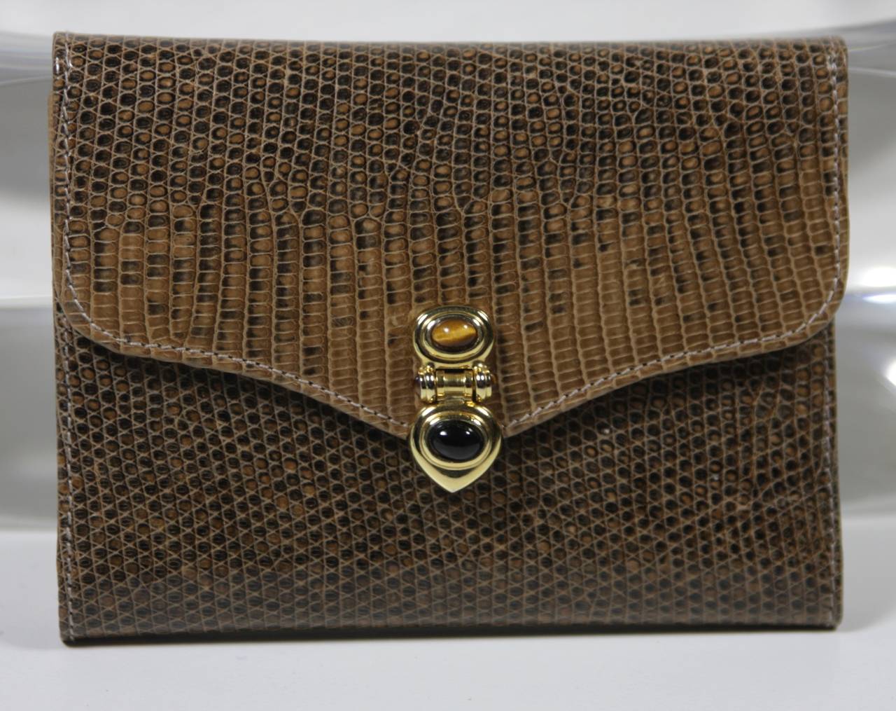 This vintage Judith Leiber is available for viewing at our Beverly Hills Boutique. We offer a large selection of evening gowns and luxury garments.

This wallet is composed of brown lizard skin and features gold hardware. The clasp is accented