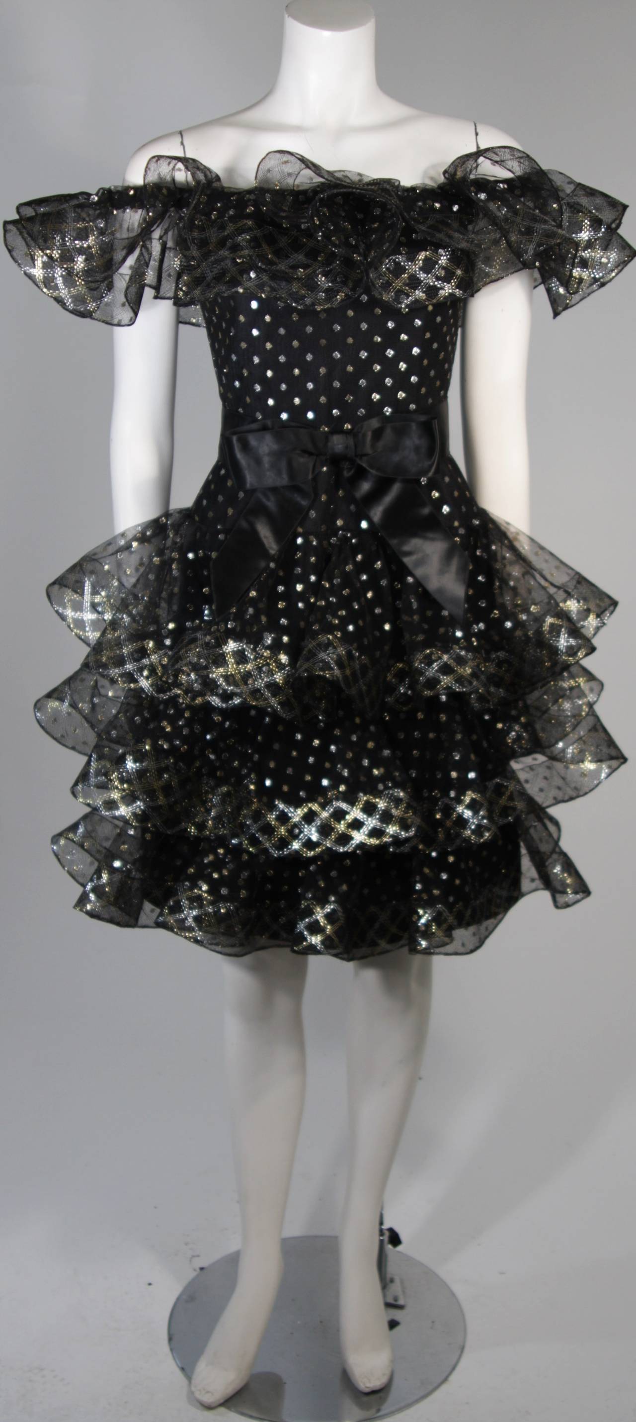 This Victor Costa cocktail dress is fabricated from layers of black mesh fabric accented with silver and gold metallic polka dots. The ruffled hem lines are slightly structured due to the 