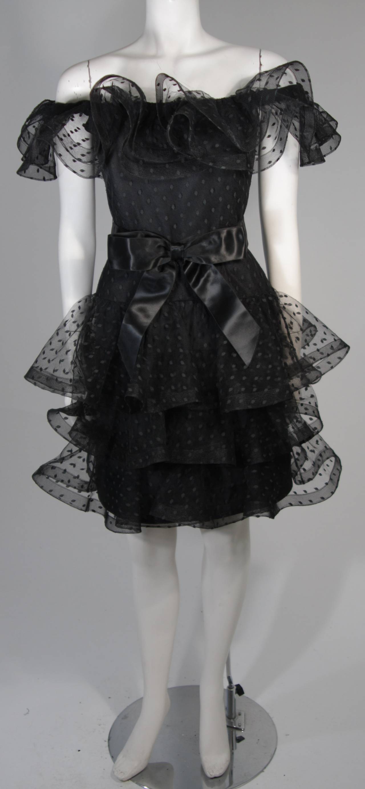 This Victor Costa cocktail dress is fabricated from layers of black mesh fabric accented with a polka dot design. The ruffled hem lines are slightly structured due to the 