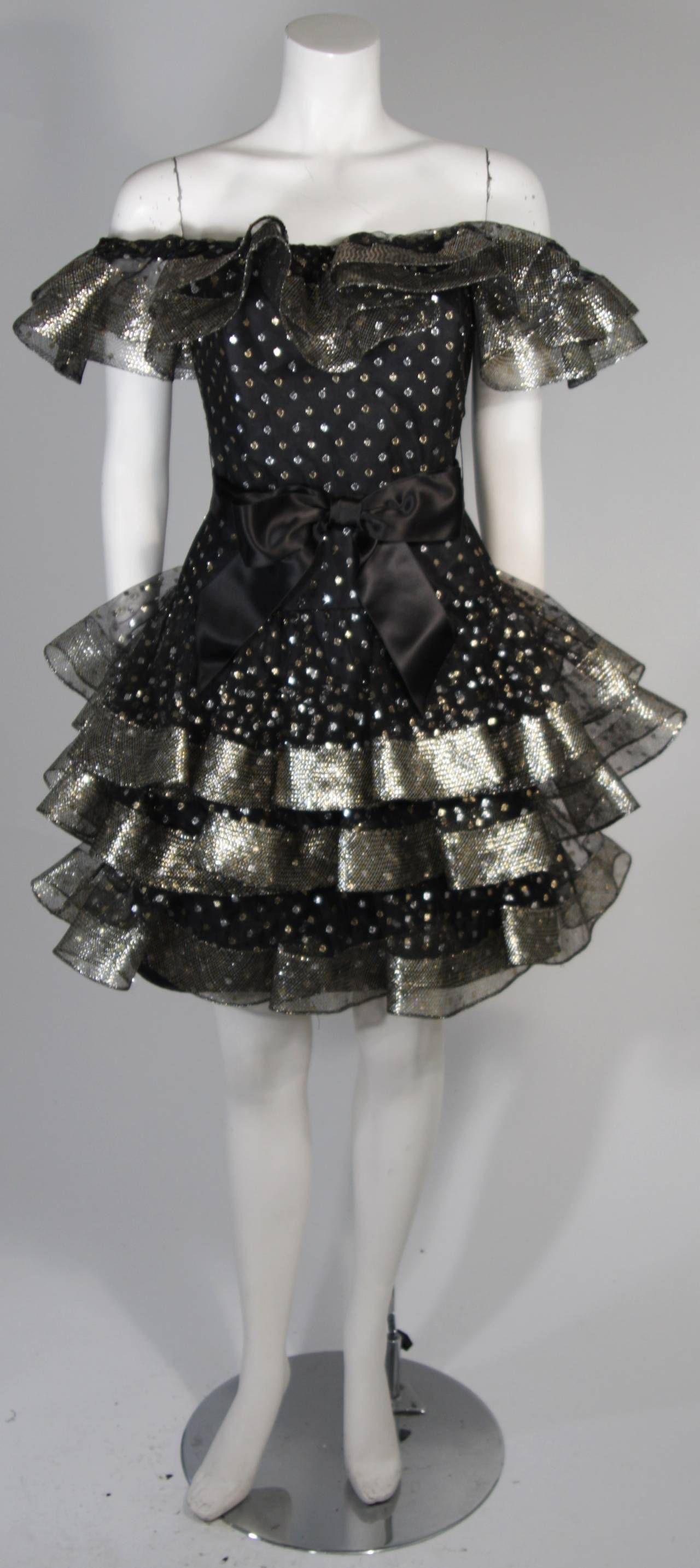 This Victor Costa cocktail dress is fabricated from layers of black mesh fabric accented with silver and gold metallic polka dots. The ruffled hem lines are slightly structured due to the 