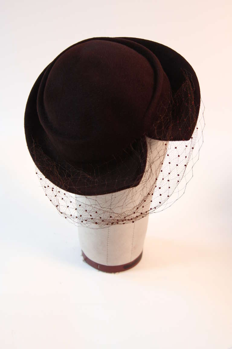 This is a great Hattie Carnegie design. The hat is composed of brown fur felt and features a split brim along with a wonderful accent of dotted netting. The netting does have a few splits through out. A magnificent hat and true to it times period of