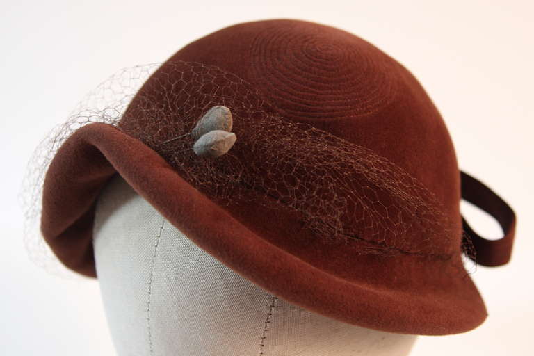 This is an original Jacques Fath design. This beautiful hat is composed of an exquisite brown fur felt. It features a circular stitch design, two hat pins, a wonderful pliable felt ribbon, and a beautifully accented netting. There a couple of tears