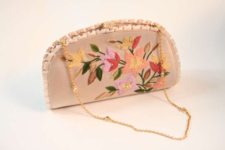 This is a Judith Leiber original design clutch. This beautiful clutch features a wonderful floral embroidered detail. The superb champagne color silk is accented with a perfect knife ruffle pleat along the edges. The purse also features a