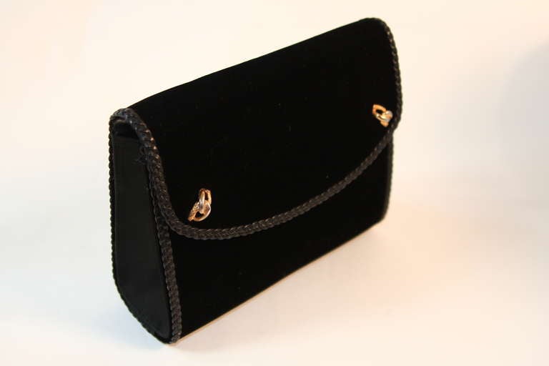 This is a Gucci black velvet clutch. The bag features a snap closure and two interior pockets. The handbag features a leather braided detail at the edge and strap. It can be worn as a clutch or strap handbag. Some of the hardware at the strap