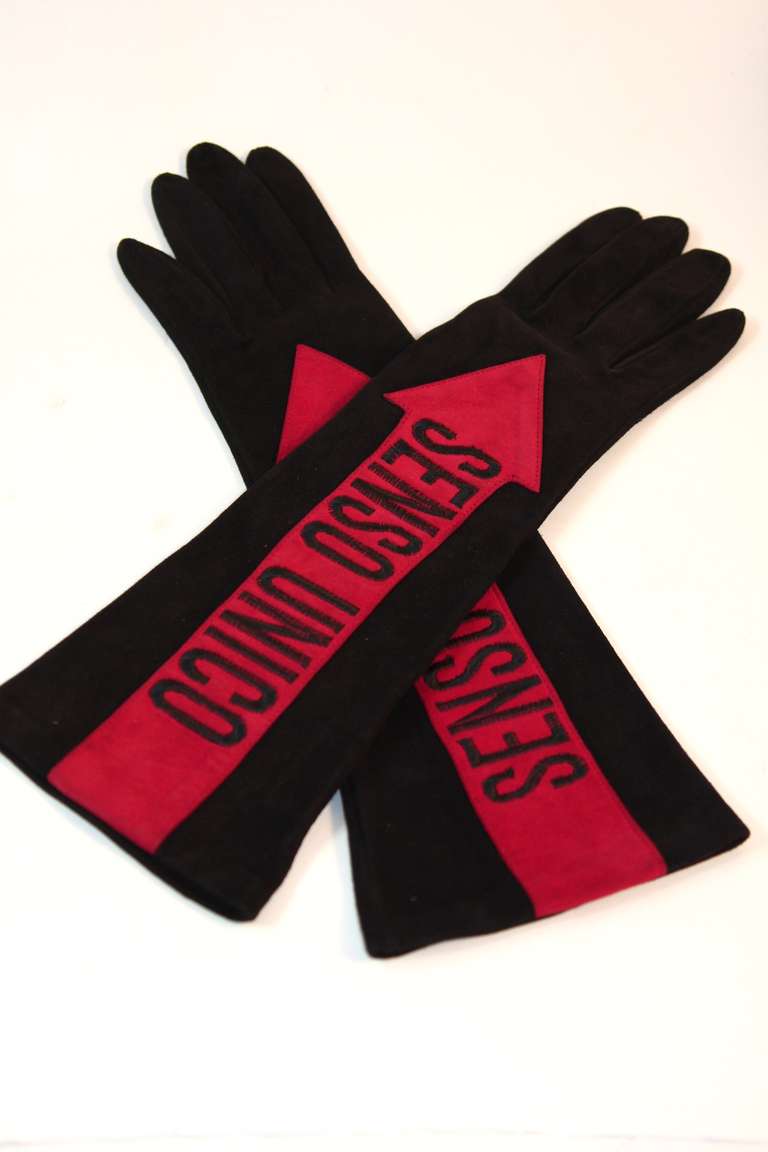 These are a pair of fabulous Moschino suede gloves. They are a wonderful black suede with contrasting red arrows and the words 