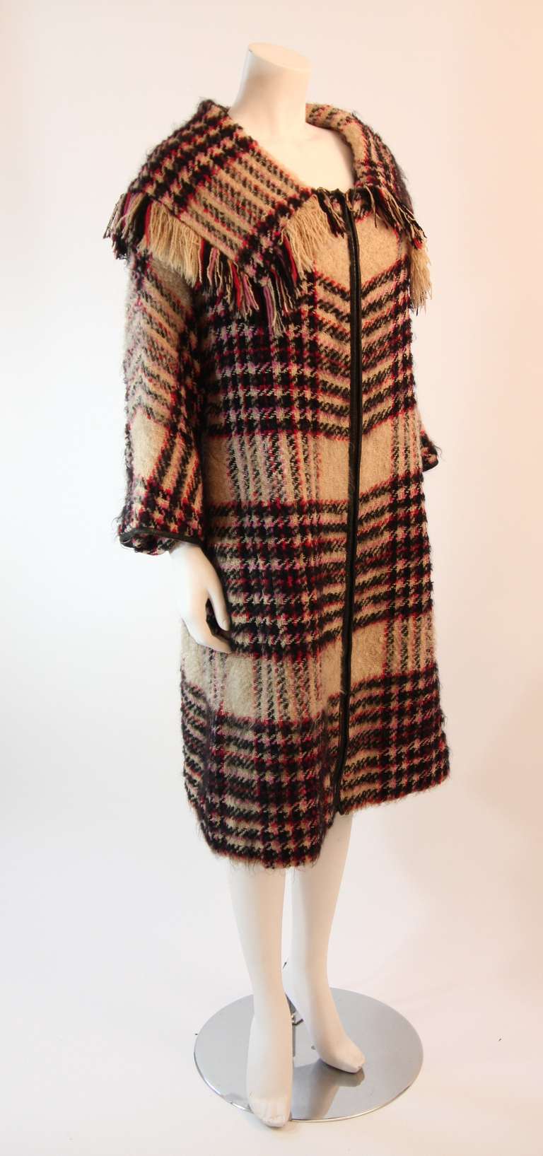This is an amazing Bonnie Cashin wool coat. The coat is a wonderful multi-colored plaid with red, pink, and black striping with an oatmeal base. The coat also features a zipper closure with leather trim, two front pockets, and 3/4 bracelet length