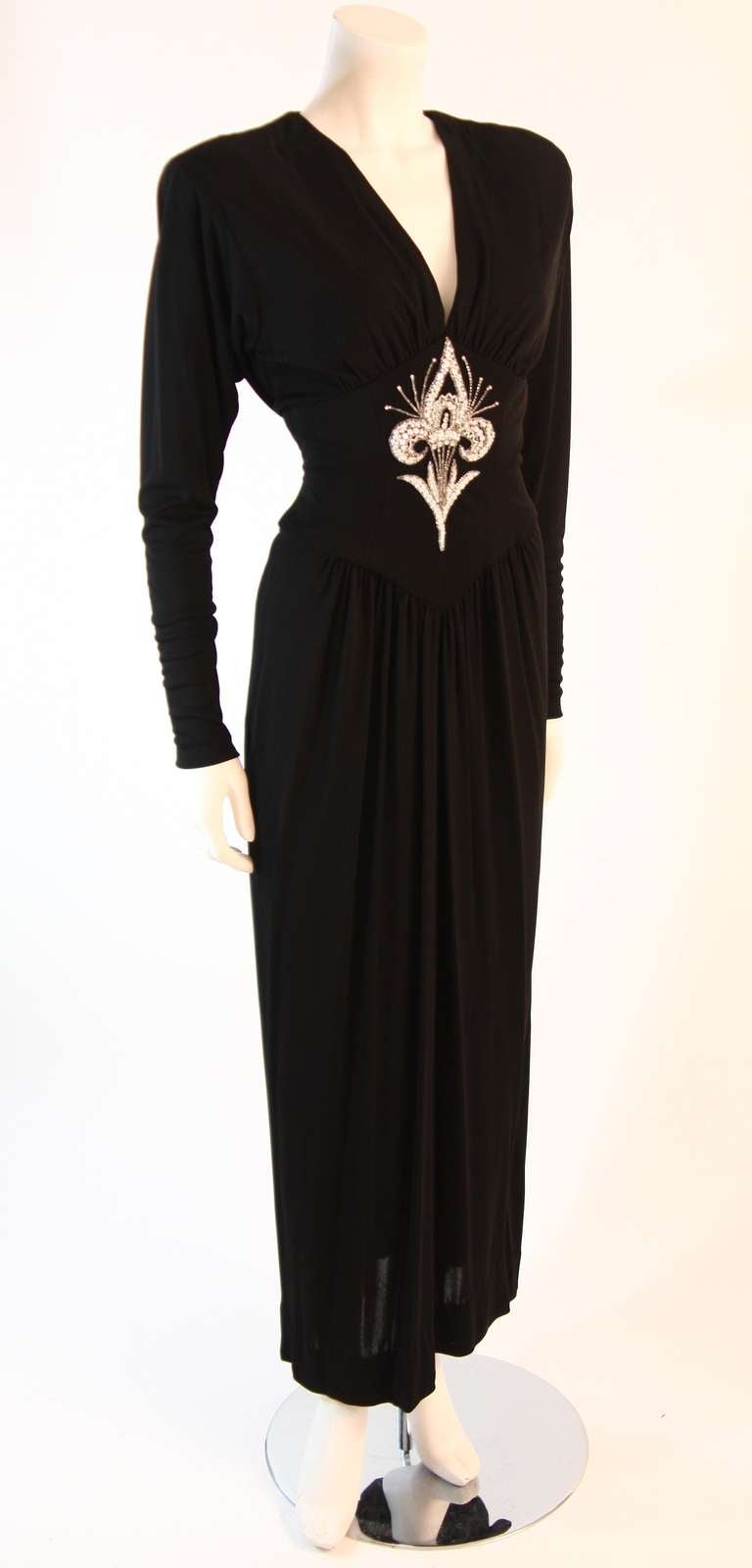This is a Bob Mackie gown. This gown features long sleeves, gathers at the bust, and draped back. The gown is composed of a stretch black outer material lined with a non-stretch material for structure and foundation. Center back zipper closure. A