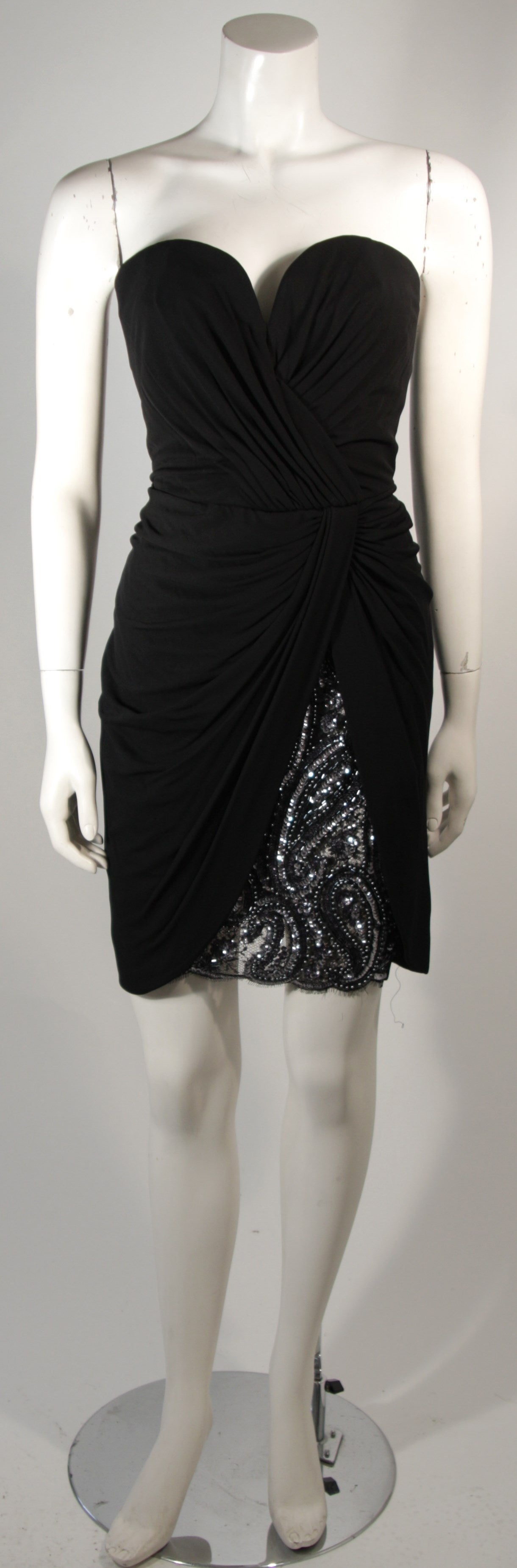 This Vicky Tiel cocktail dress is composed of a black viscose and rayon blend jersey. There are gathers throughout and a sequin detail (silver and black) at the hem. The bodice features boning for structure and a side zipper closure for ease of