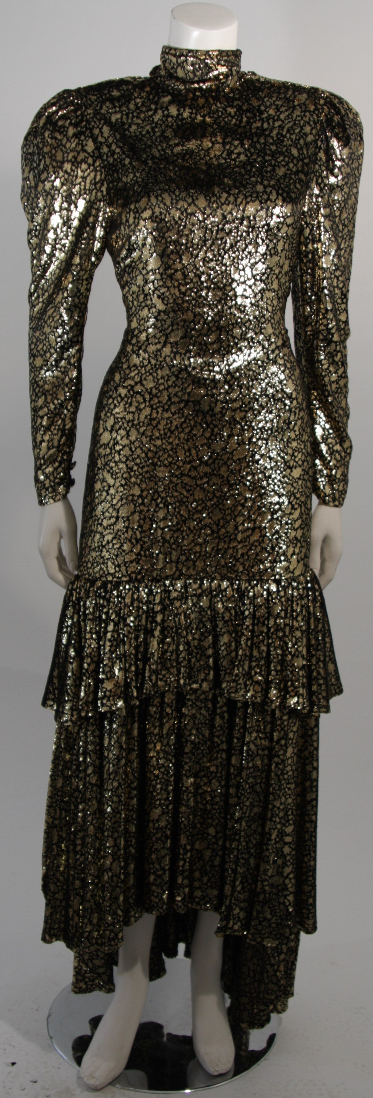 This gown is composed of a black and gold metallic fabric with the properties of velvet. There are long sleeve with gathers at the shoulders and a tiered skirt. There is a center back zipper closure for ease of access. In excellent condition, comes