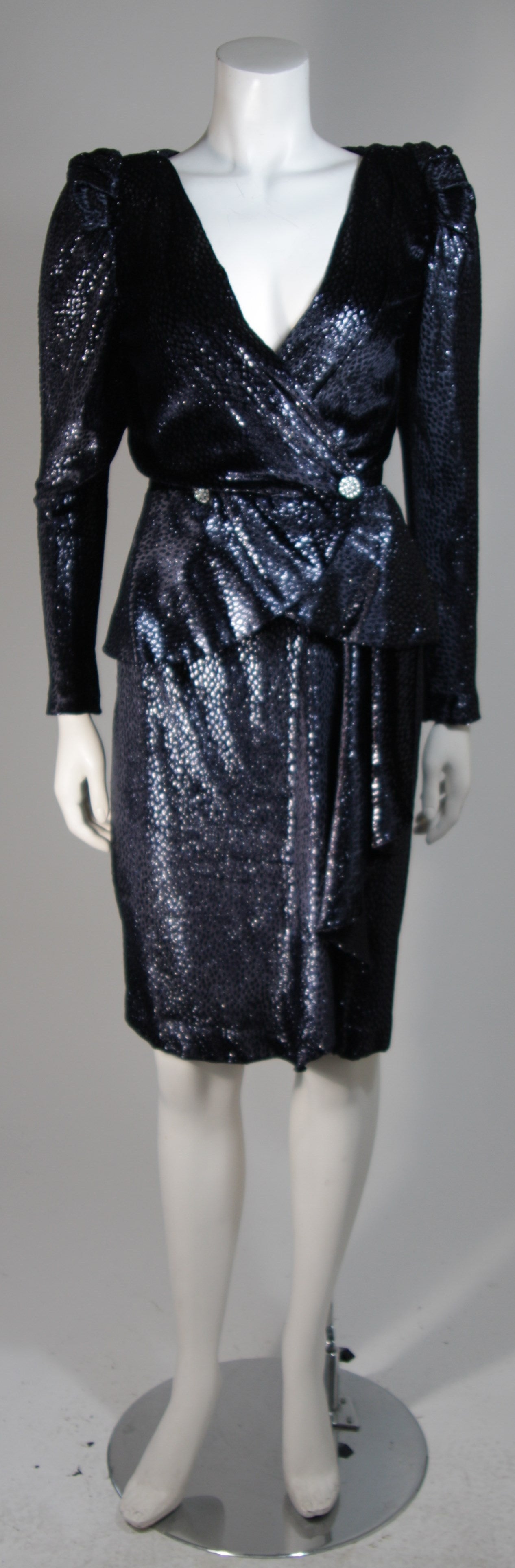 This Vicky Tiel suit is composed of a textured navy silk twill and features metallic/reflective properties. The jacket features a center front button fastening, padding at the shoulders, and a peplum waist. The skirt has a figure hugging silhouette