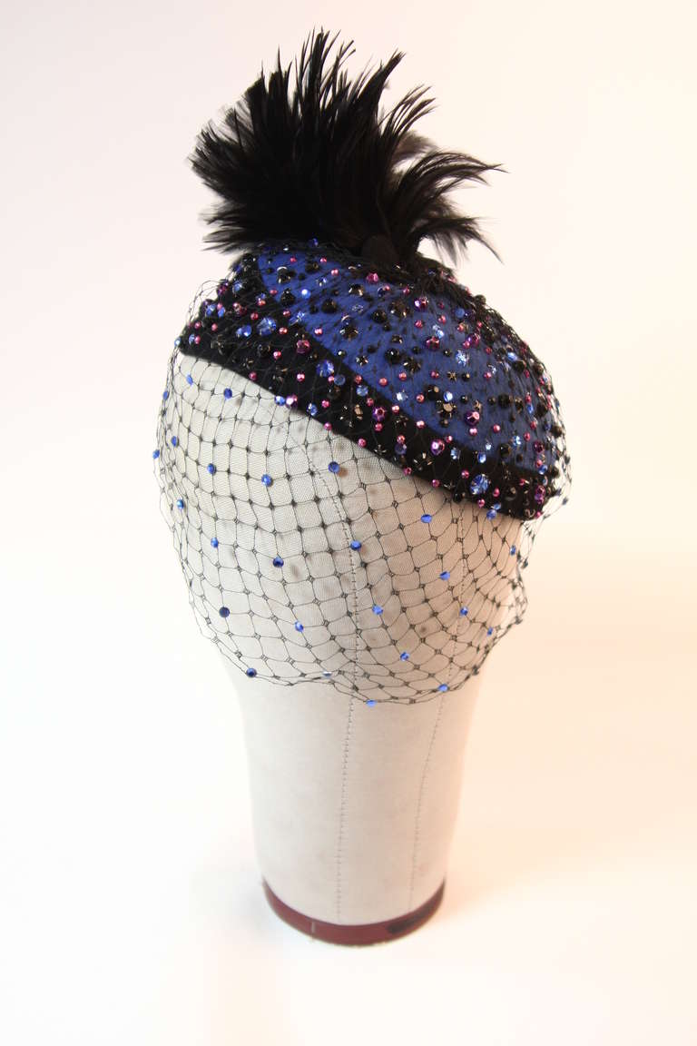 This is a fabulous Frank Olive hat. This is delightful blue and black wool hat is embellished with an array of blue, black, and pink rhinestones. The hat features a beautiful pop of feathers and a hat pin. It is stunning and a beautiful addition to