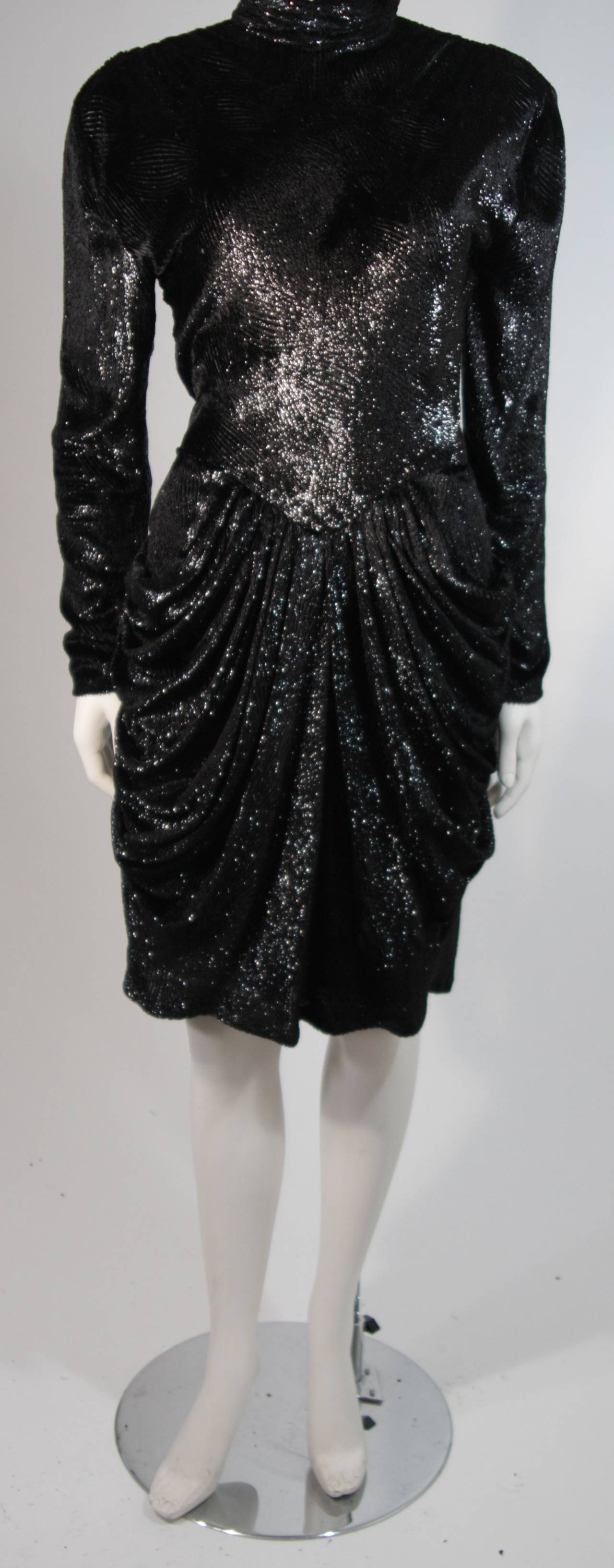 This Vicky Tiel cocktail dress is composed of a lightweight silky black metallic velvet.
There are gathers cascading from the waist and padded shoulders. There is a center back button closure for ease of access. In excellent condition. Made in