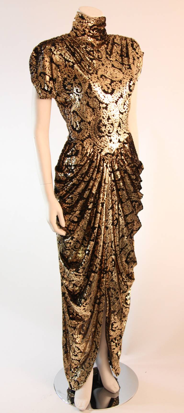 This is a spectacular Vicky Tiel gown. This amazing gown is composed of a fantastic gold and black burnout Panne velvet fabric. The gown features a drop waist, hip draping, shoulder pads, and high neck. The back is equally as flattering as the front