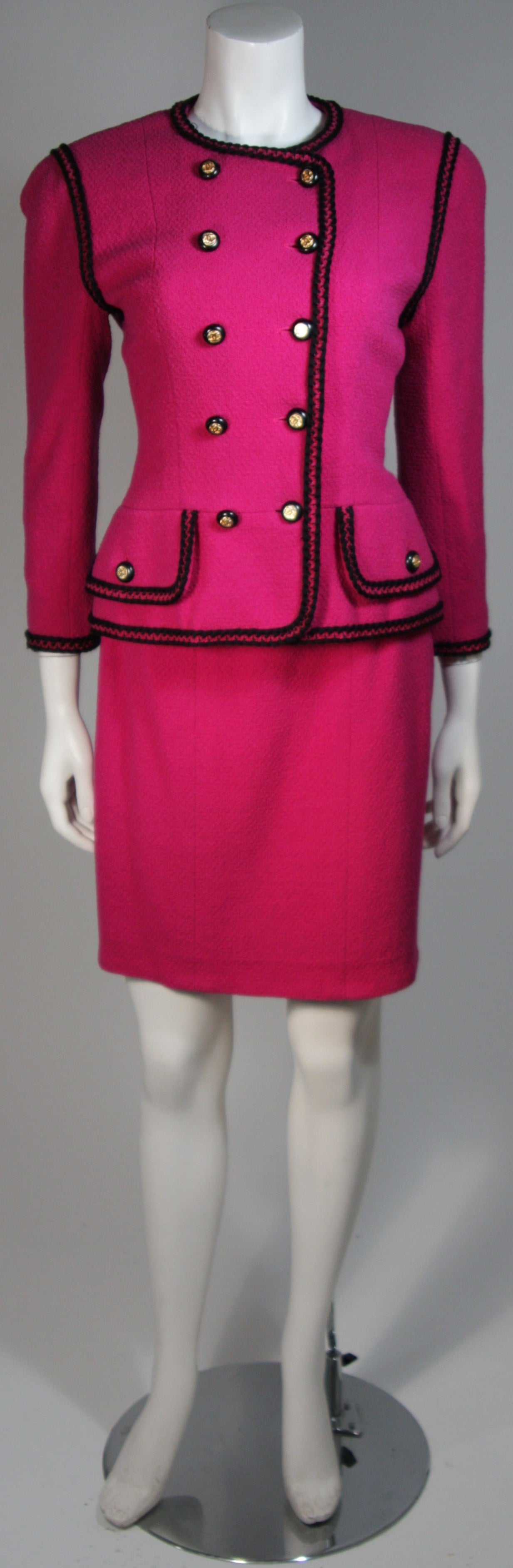 This Chanel iconic fuchsia and black jacket and skirt set by Chanel, from the 1980's. The jacket is double breasted with gold and black logo buttons on the front, pockets, and cuffs.

Please review the measurements provided below to ensure a