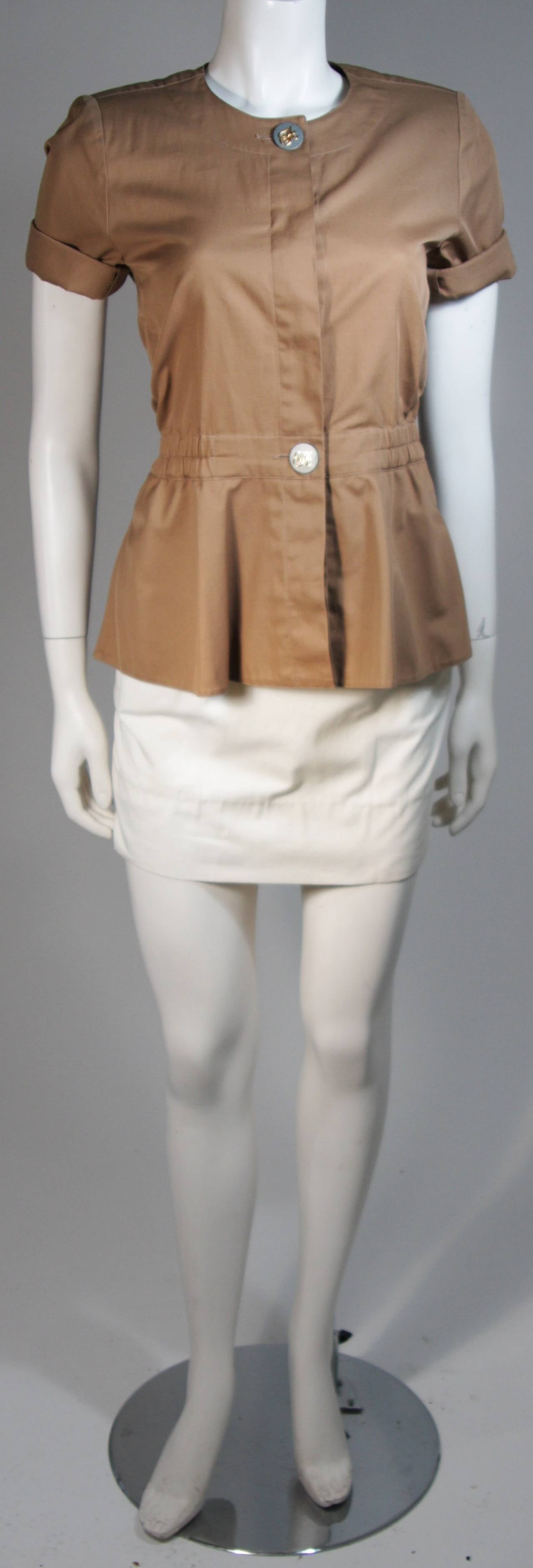 This Hermes skirt suit is composed of a white and camel khaki combination. The jacket/blouse has center front button closures, and an elastic waist detail. The skirt has a zipper closure with front pockets and pleats. In excellent vintage condition.