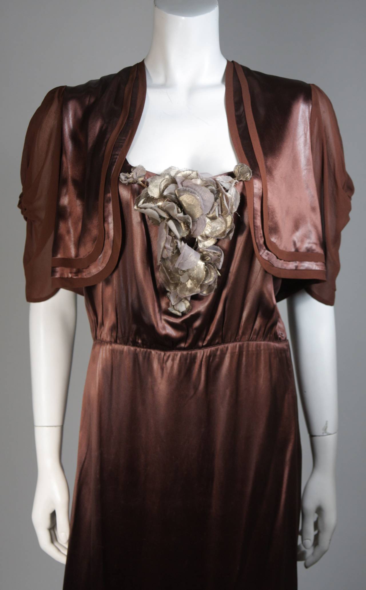 This Madame Eme set is composed of a brown silk and features a floral accent. There are side hook and eye closures on the dress. The bolero has an open style with draped sleeves. In excellent vintage condition.

**Please cross-reference