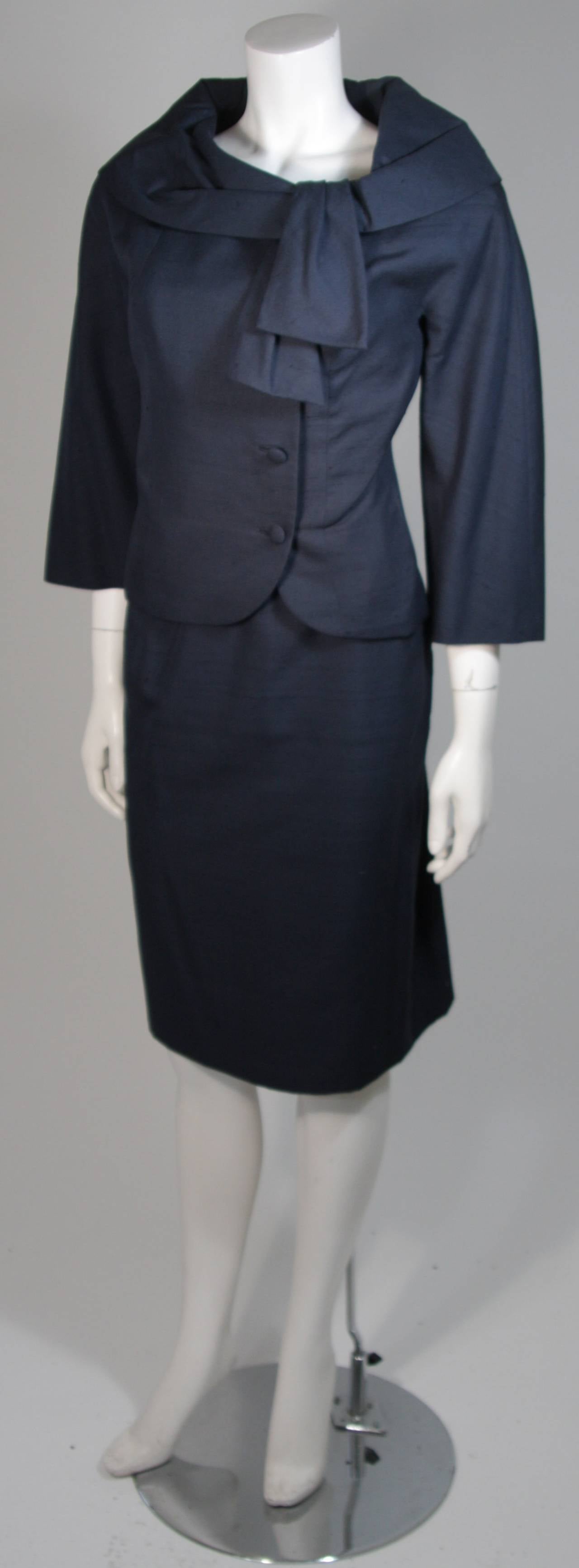 This fabulous Don Loper jacket, comprised of navy silk shantung, features a perfectly placed portrait collar, three-quarter length bracelet sleeves, and off-center covered buttons down the front. 
Matching navy silk pencil skirt. 
Both pieces are