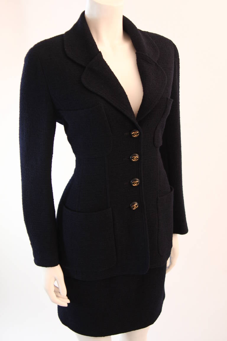 Classic Chanel Boutique 1993 Cruise collection navy boucle wool 4 pocket jacket with a matching straight skirt. The jacket and skirt are both accented with navy and gold CC logo buttons. Both pieces are lined in navy silk and are in excellent
