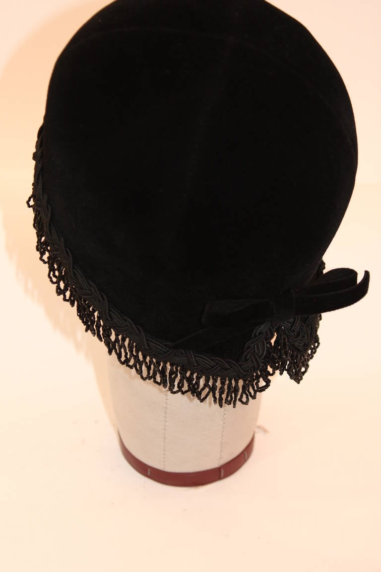 This is a spectacular Christian Dior cloche hat. This hat is composed of a wonderful black velvet accented with a beaded fringe trim and delicate little bow at the split which can be worn to the side or at the back. 
Circa 1960's. Made in France.